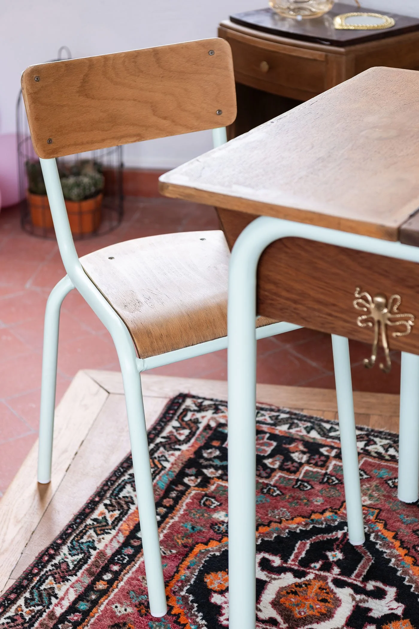 Détail d’une chaise d’écolier vintage restaurée, structure métal vert amande et assise en bois, photographiée dans l’atelier Meliwood.
