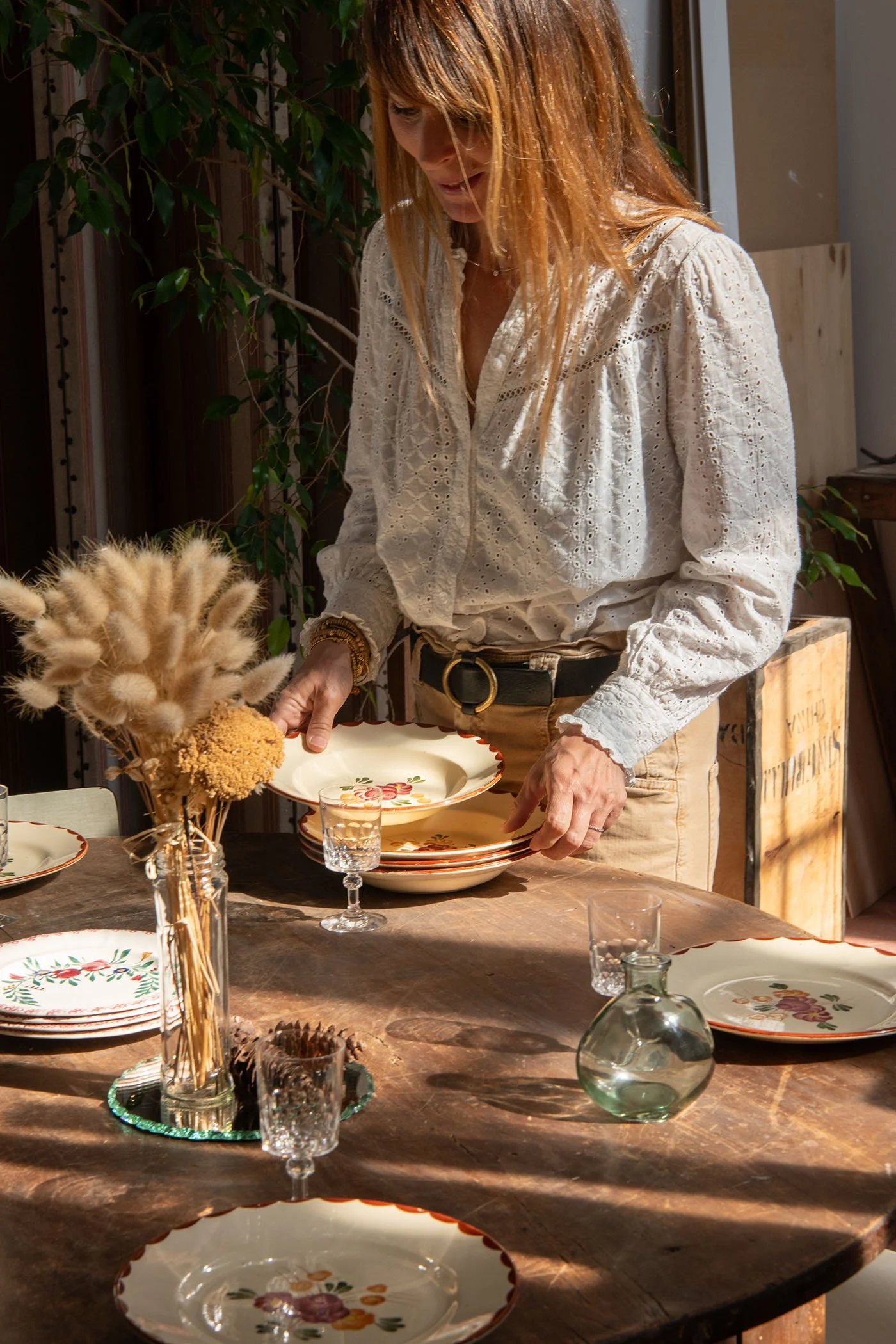 Amélie disposant des assiettes vintage peintes à la main sur une table ancienne restaurée dans son atelier.