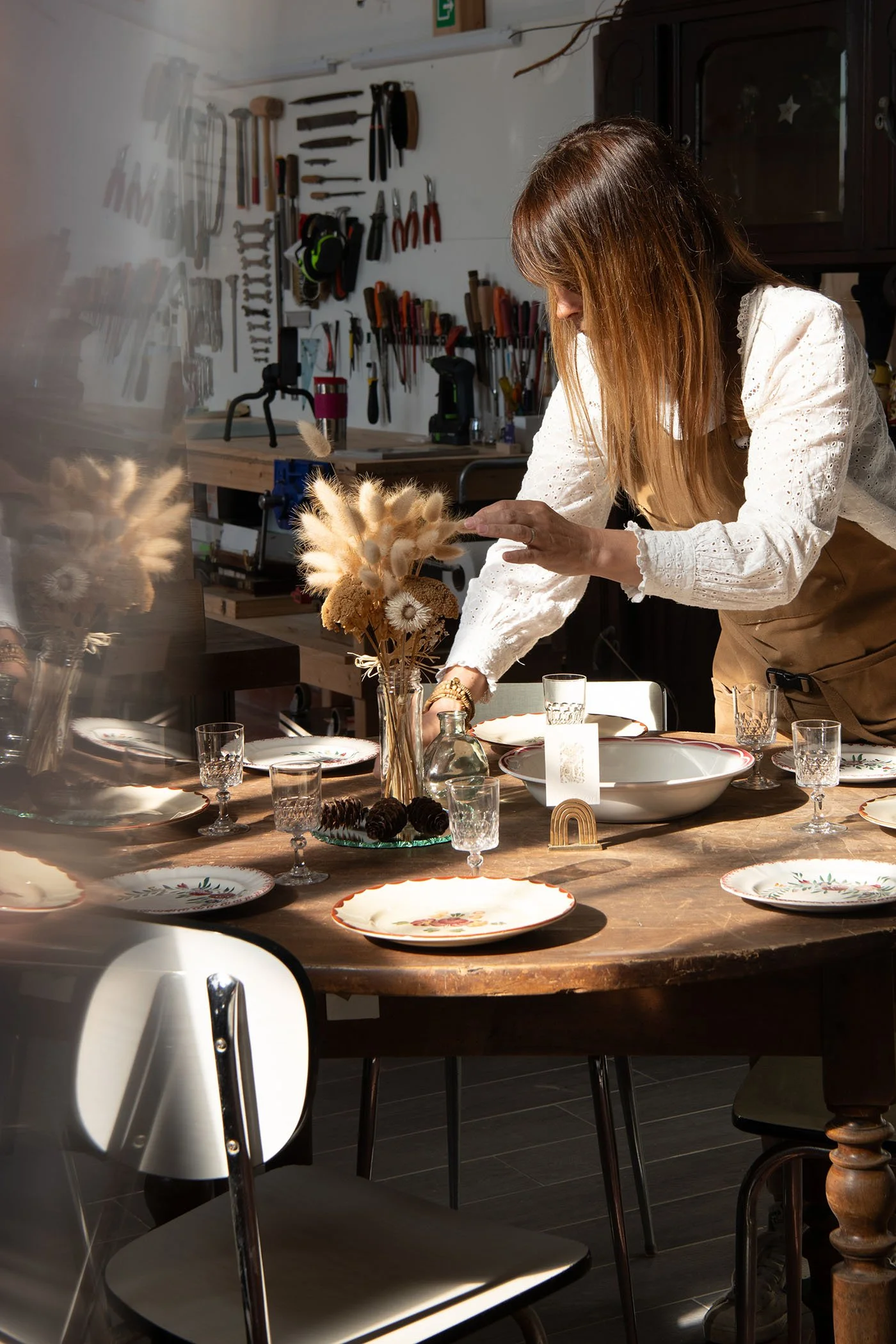 Amélie dressant une table vintage dans son atelier Meliwood, disposant de la vaisselle ancienne et un bouquet séché sur un meuble restauré.