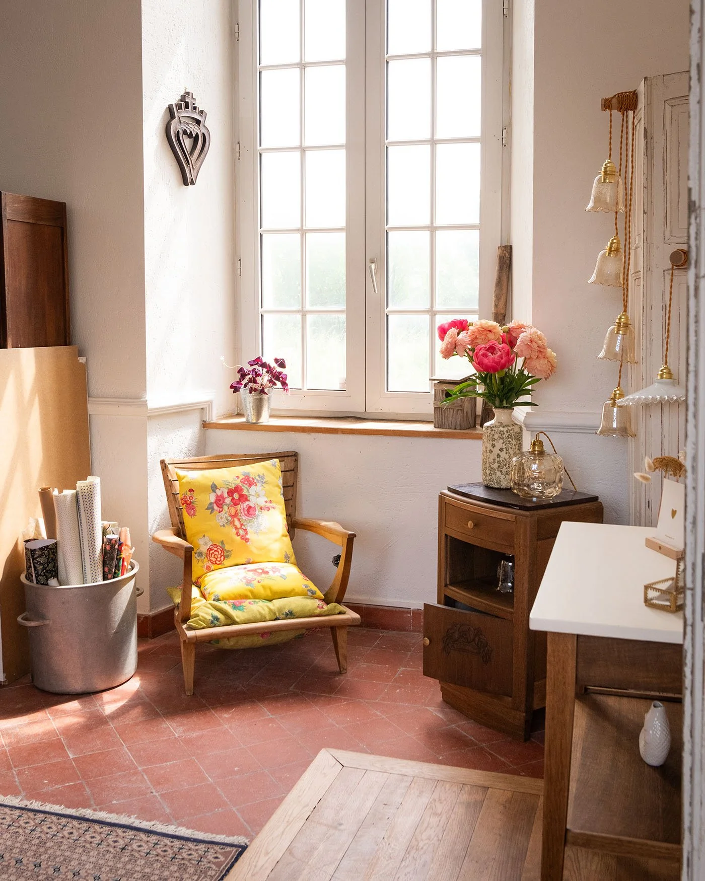 Coin atelier lumineux avec fauteuil ancien restauré, coussin rétro fleuri, luminaires vintage et objets chinés dans l’atelier Meliwood.