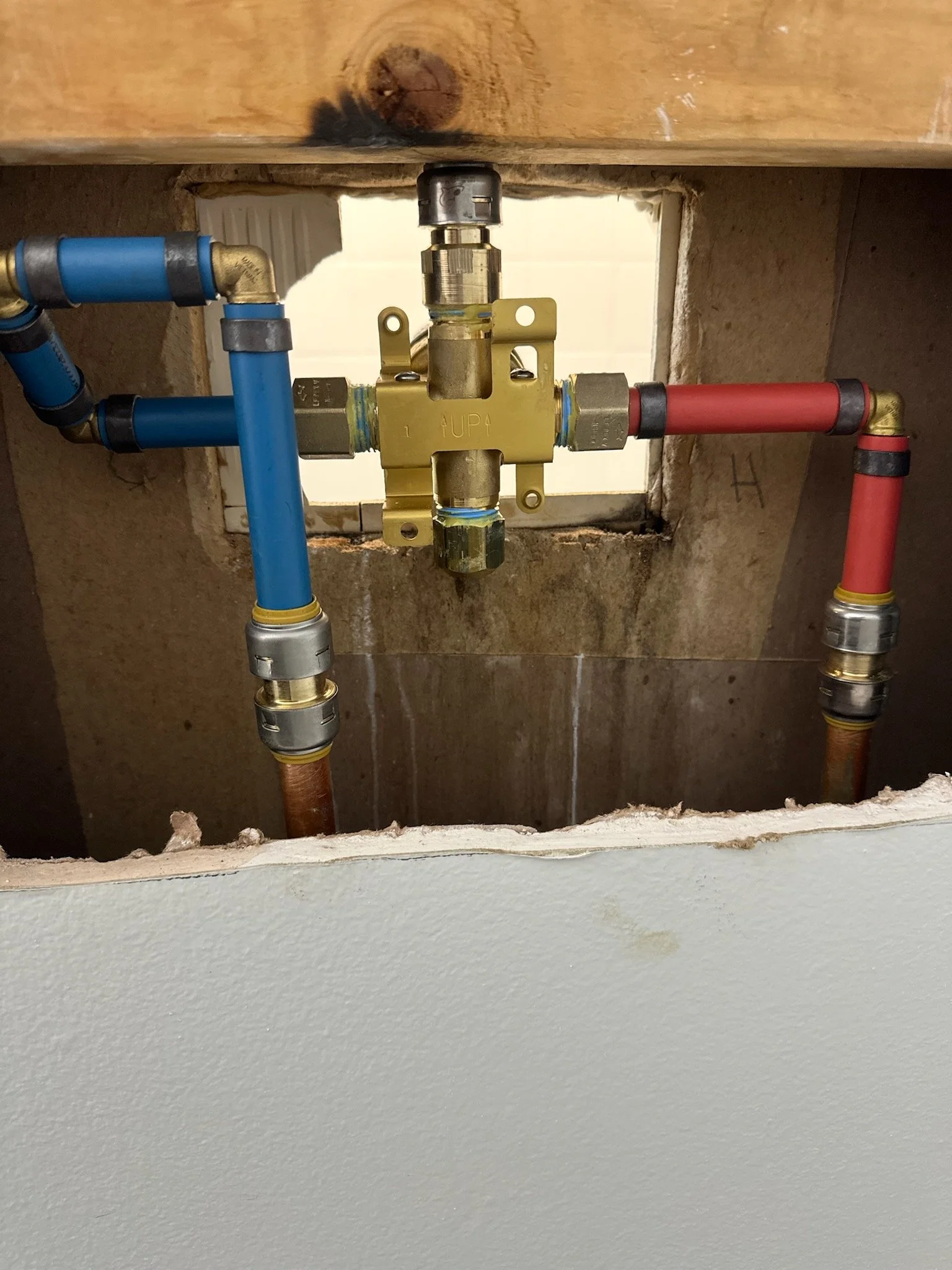 Plumbing pipes and valve in wall cavity, with blue and red pipes indicating hot and cold water lines.