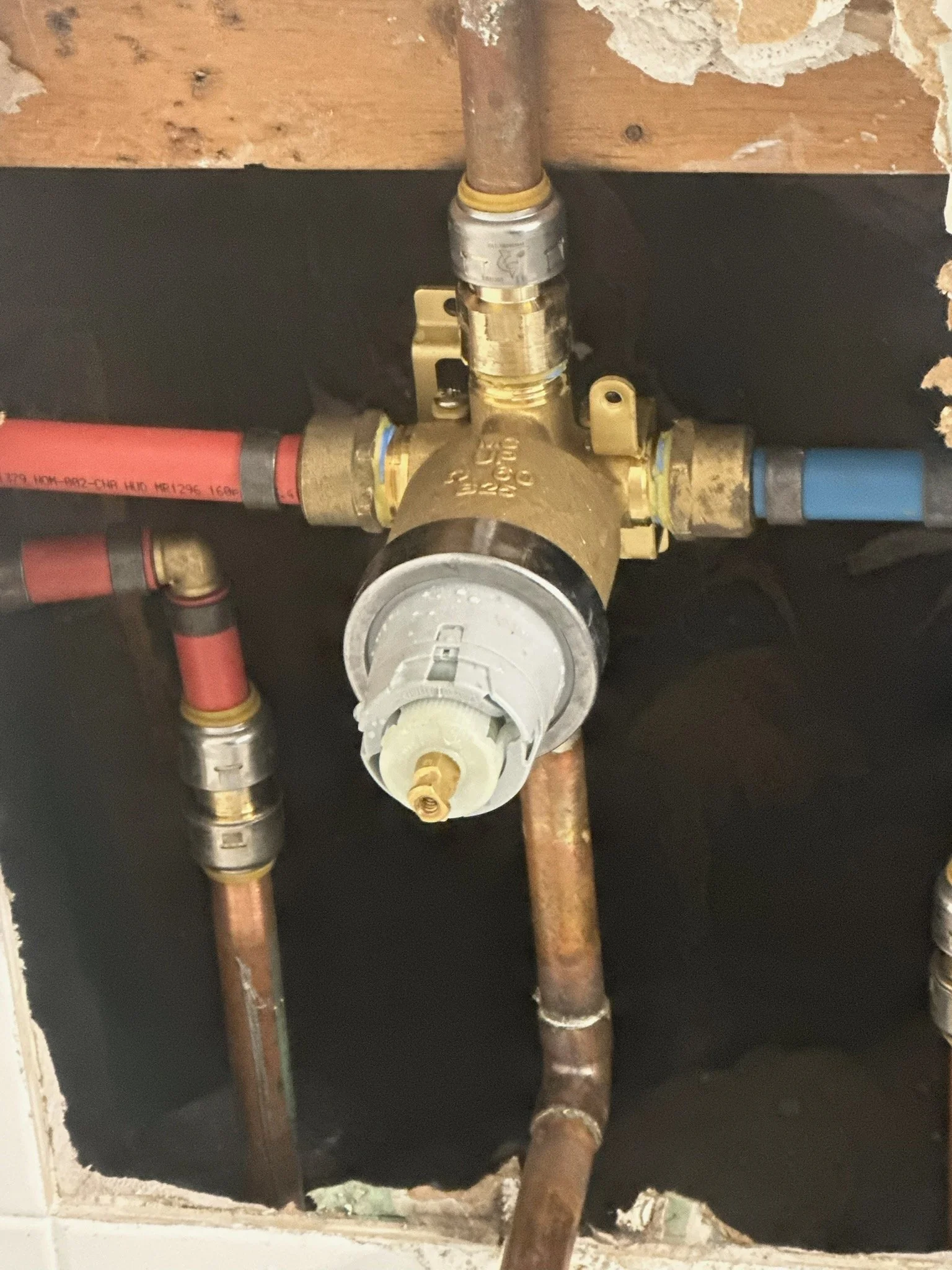 A plumbing water shut-off valve with copper pipes and red and blue PEX tubing in a wall opening.