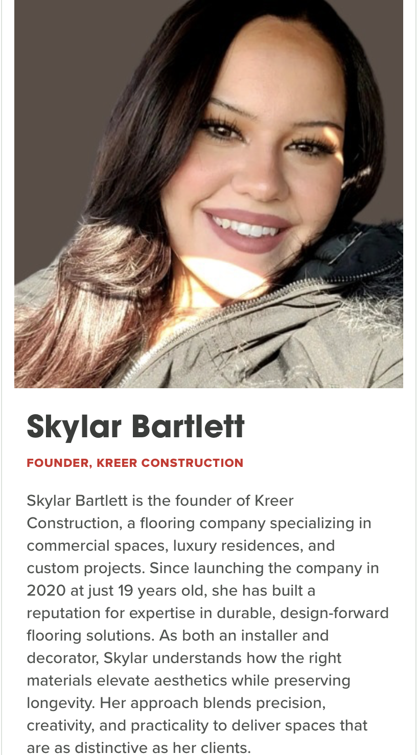 A woman with long, dark brown hair smiling at the camera, wearing a dark-colored jacket, with sunlight lighting her face.