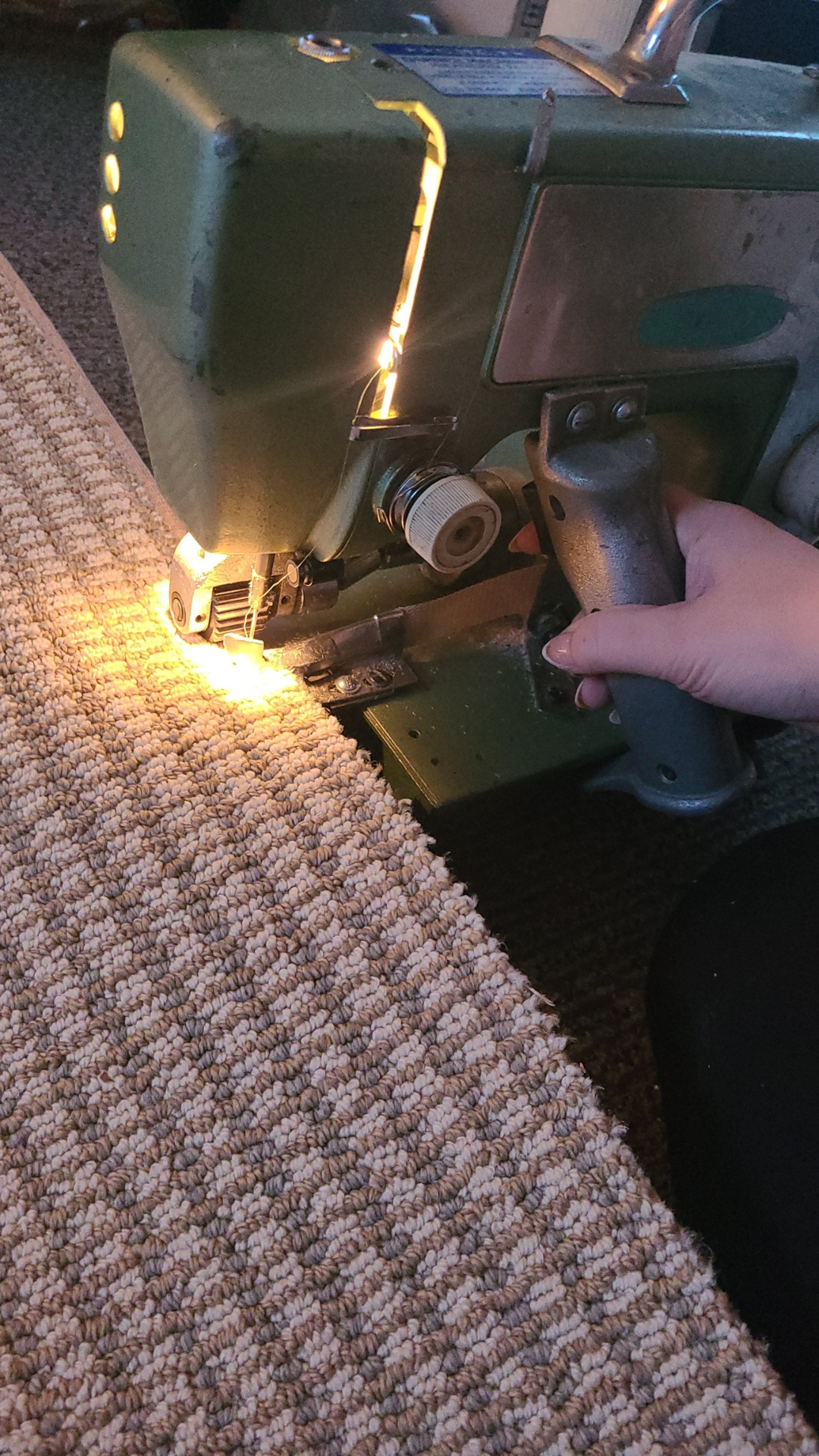 Person operating a vintage green sewing machine, stitching a beige textured fabric.