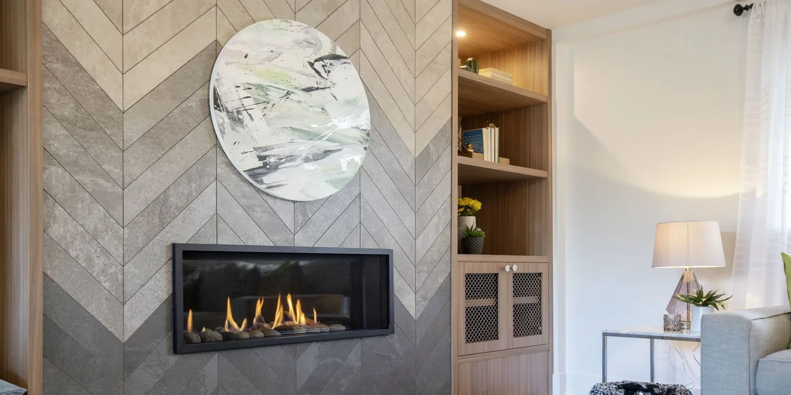 Living room with a modern wall-mounted fireplace, abstract art above it, wooden built-in shelves to the right, and a sofa with a table lamp nearby.