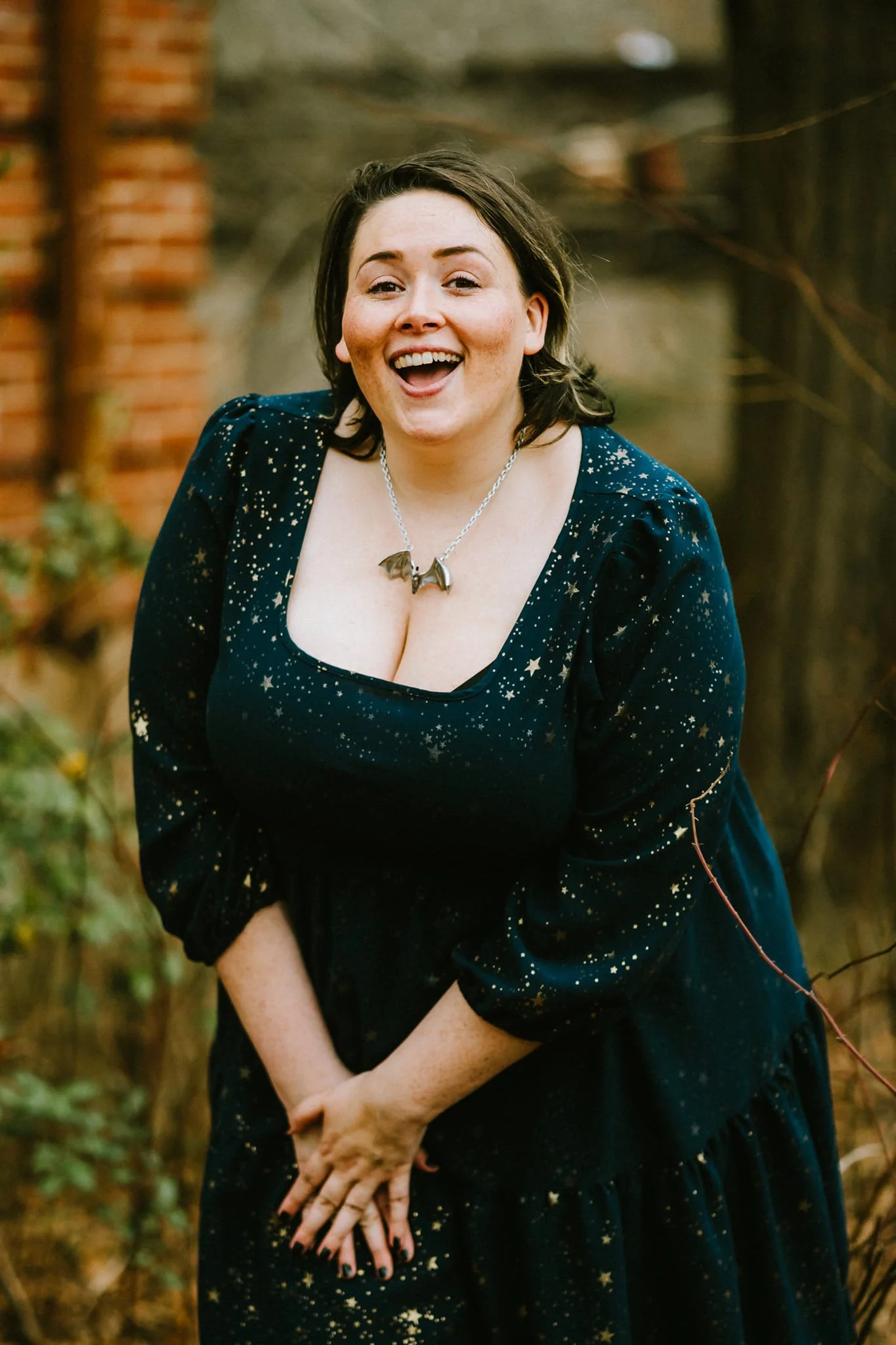 A woman with dark hair wearing a dark dress with a starry pattern, smiling and posing outdoors.