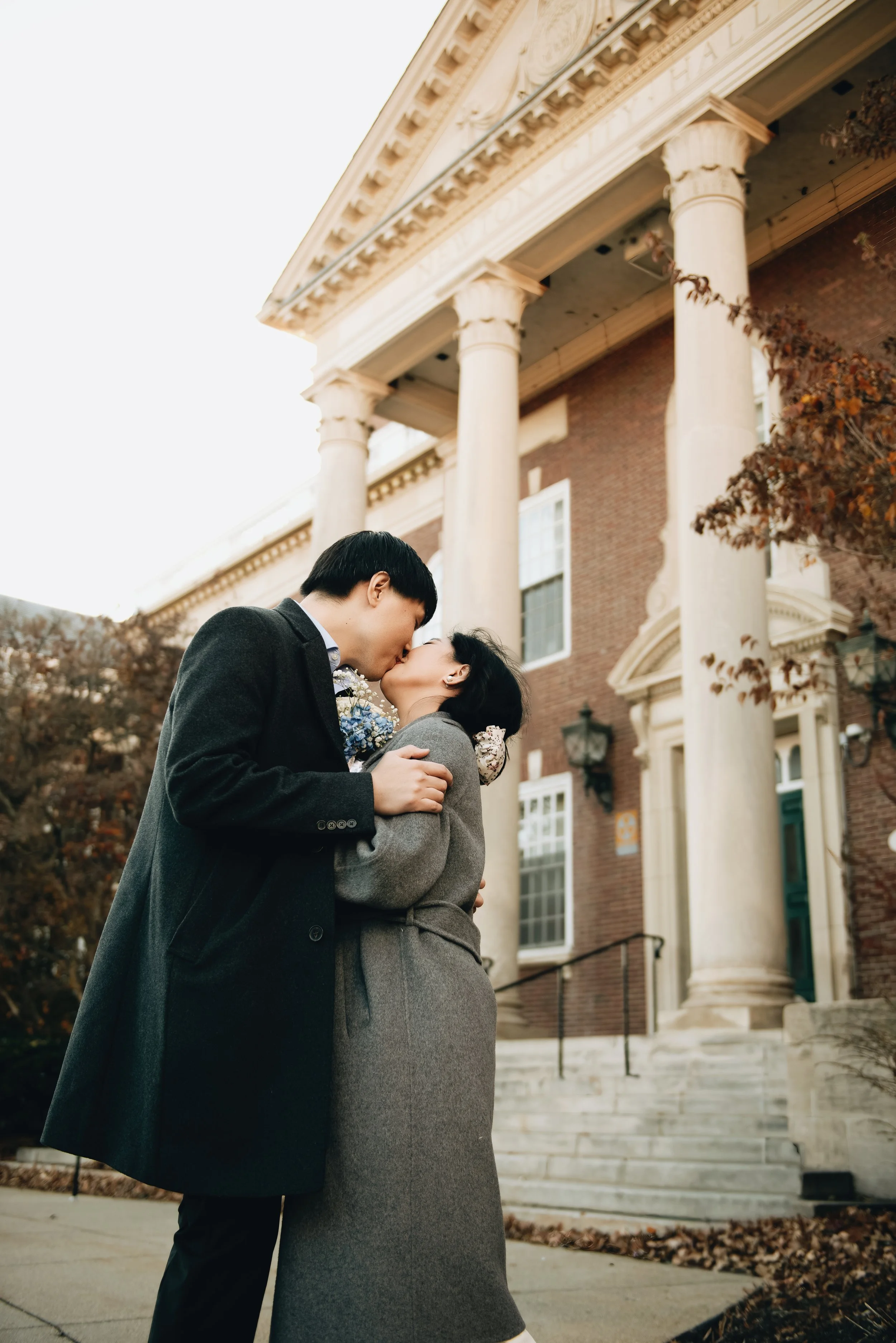 A couple kissing in front of a historic building with large columns.