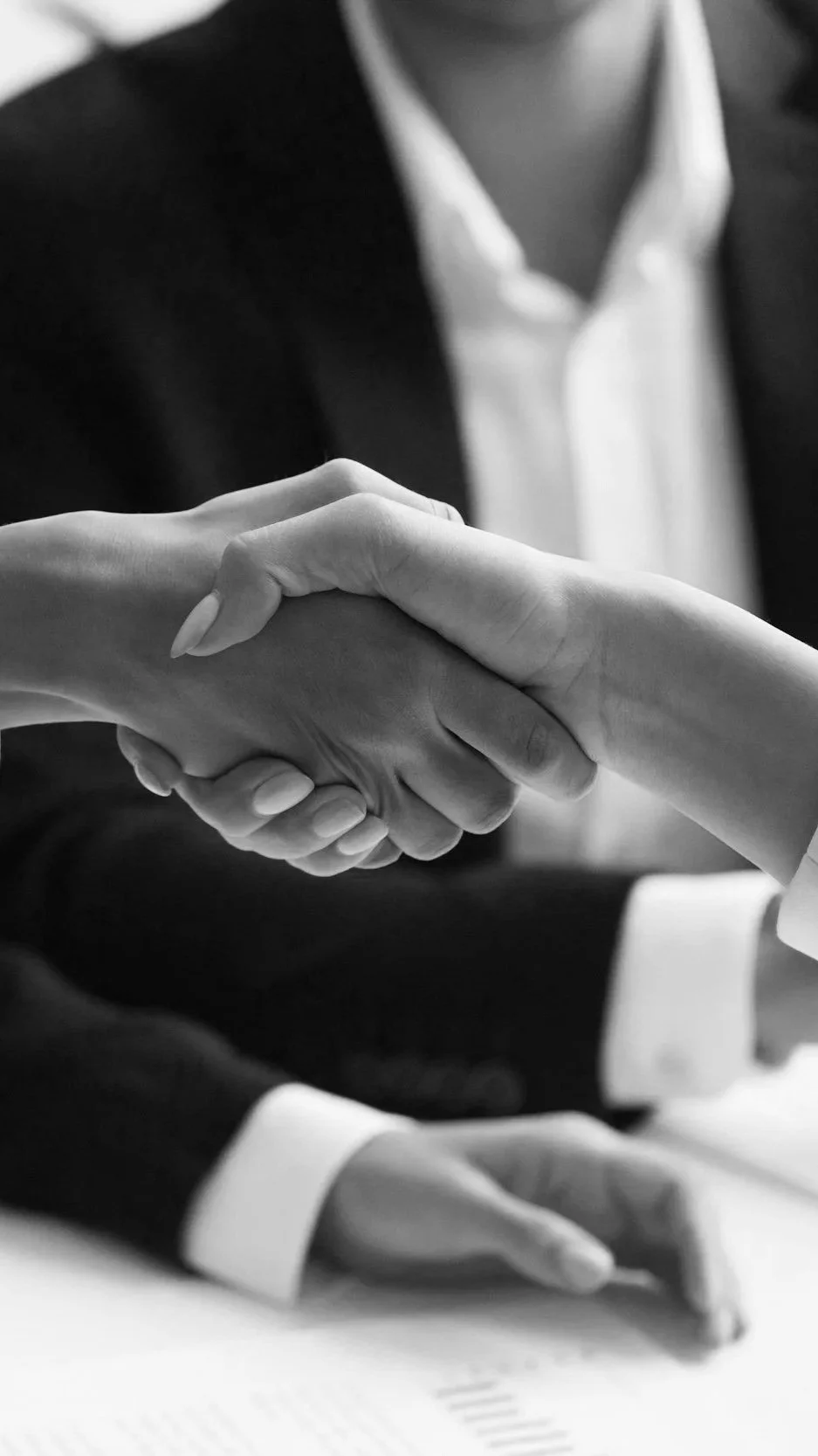 Close-up of a handshake between two people dressed in business attire, black-and-white photo.