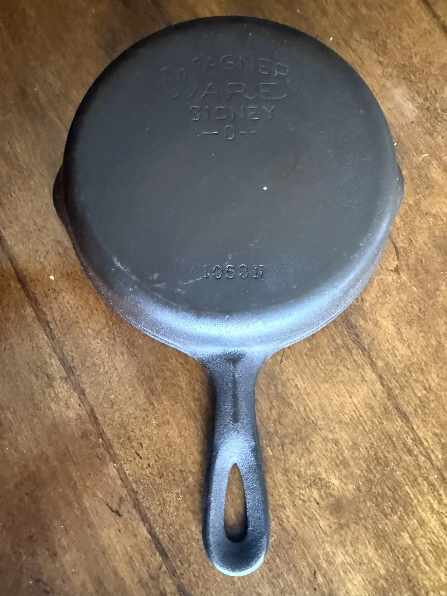 A black cast iron skillet pan on a wooden surface. The bottom has embossed text including words 'Lodge' and 'Made in U.S.A.'.