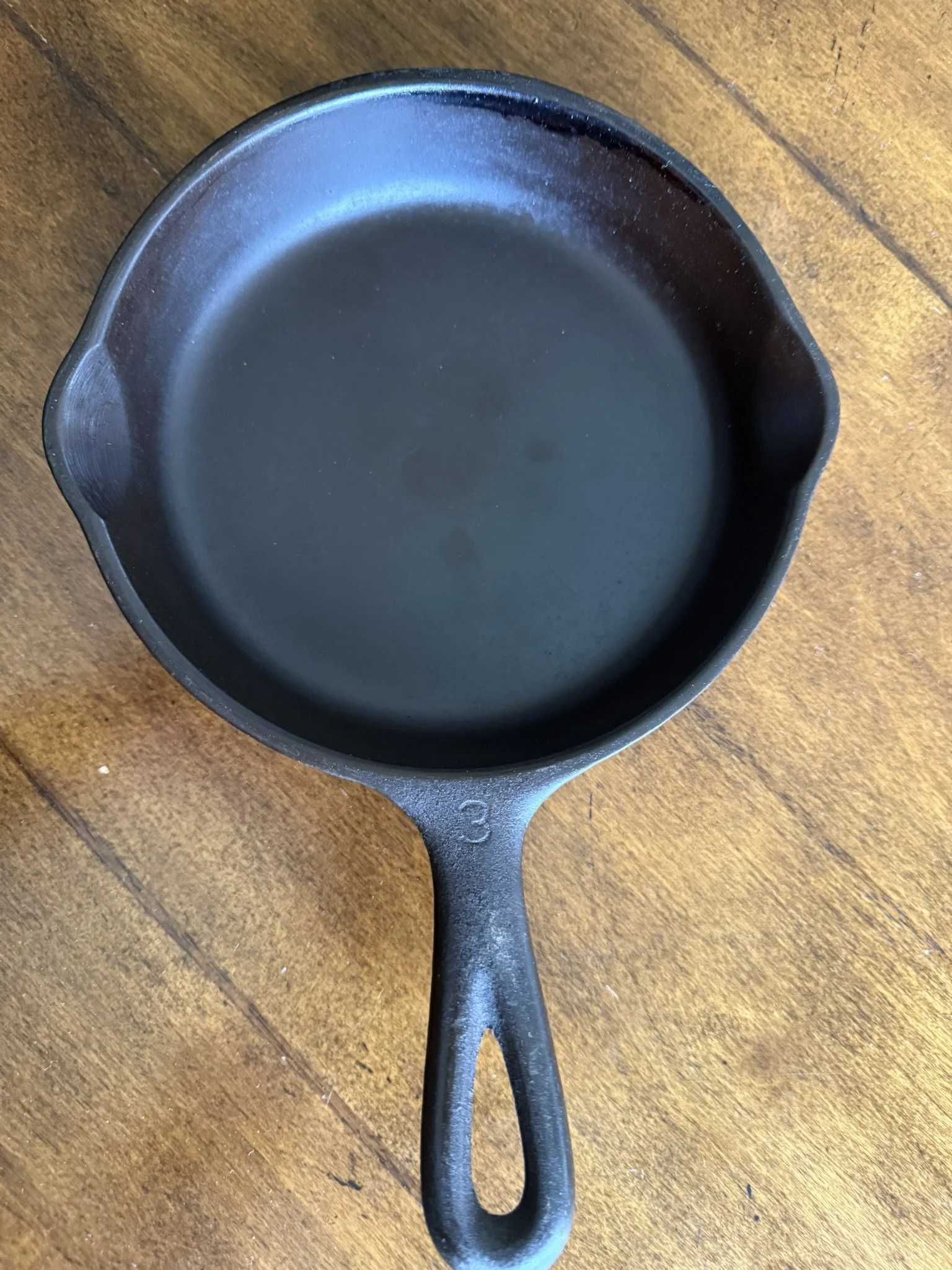 A black cast iron skillet filled with oil resting on a wooden surface.