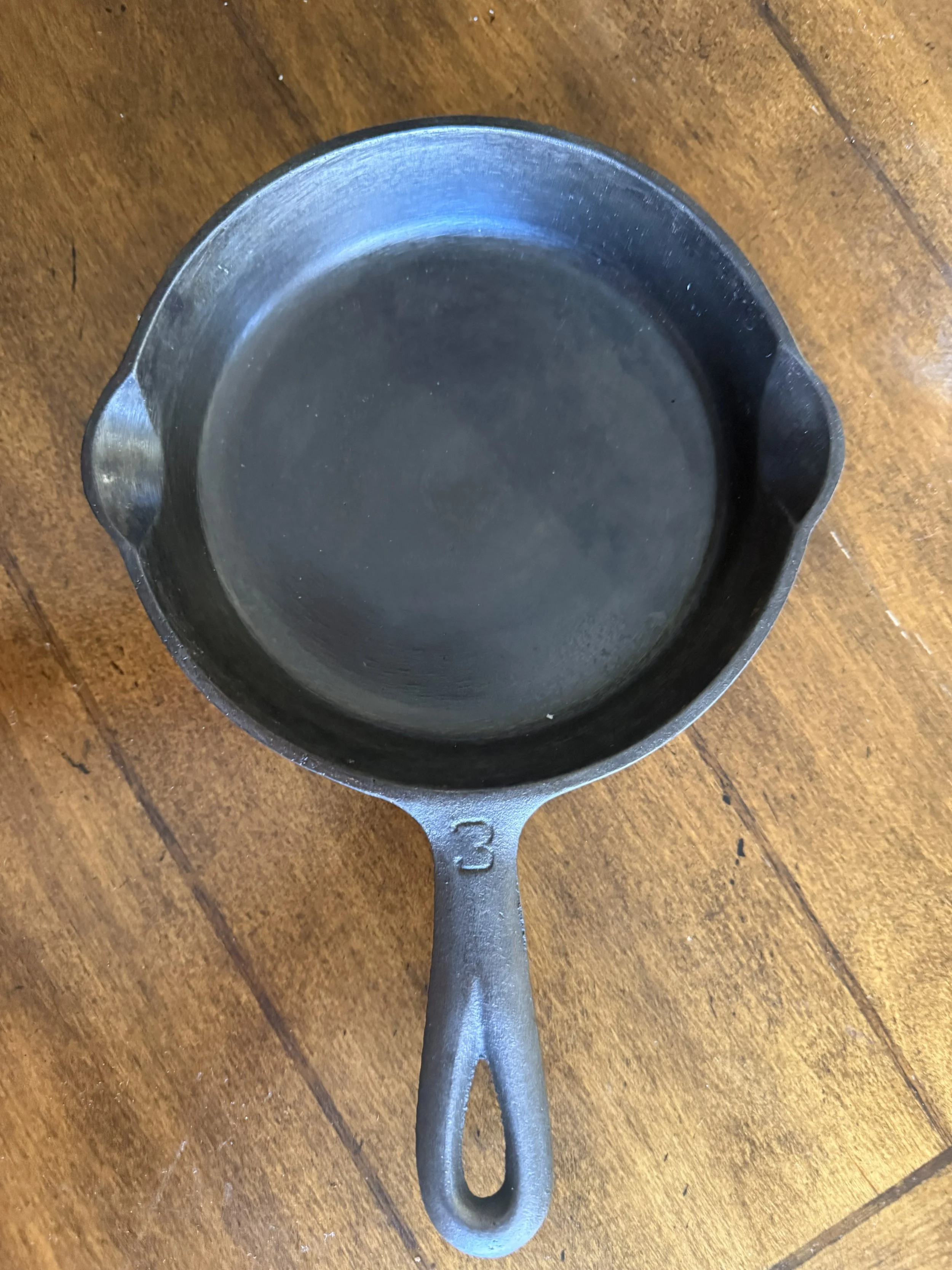Empty cast iron skillet pan on a wooden surface, viewed from above.