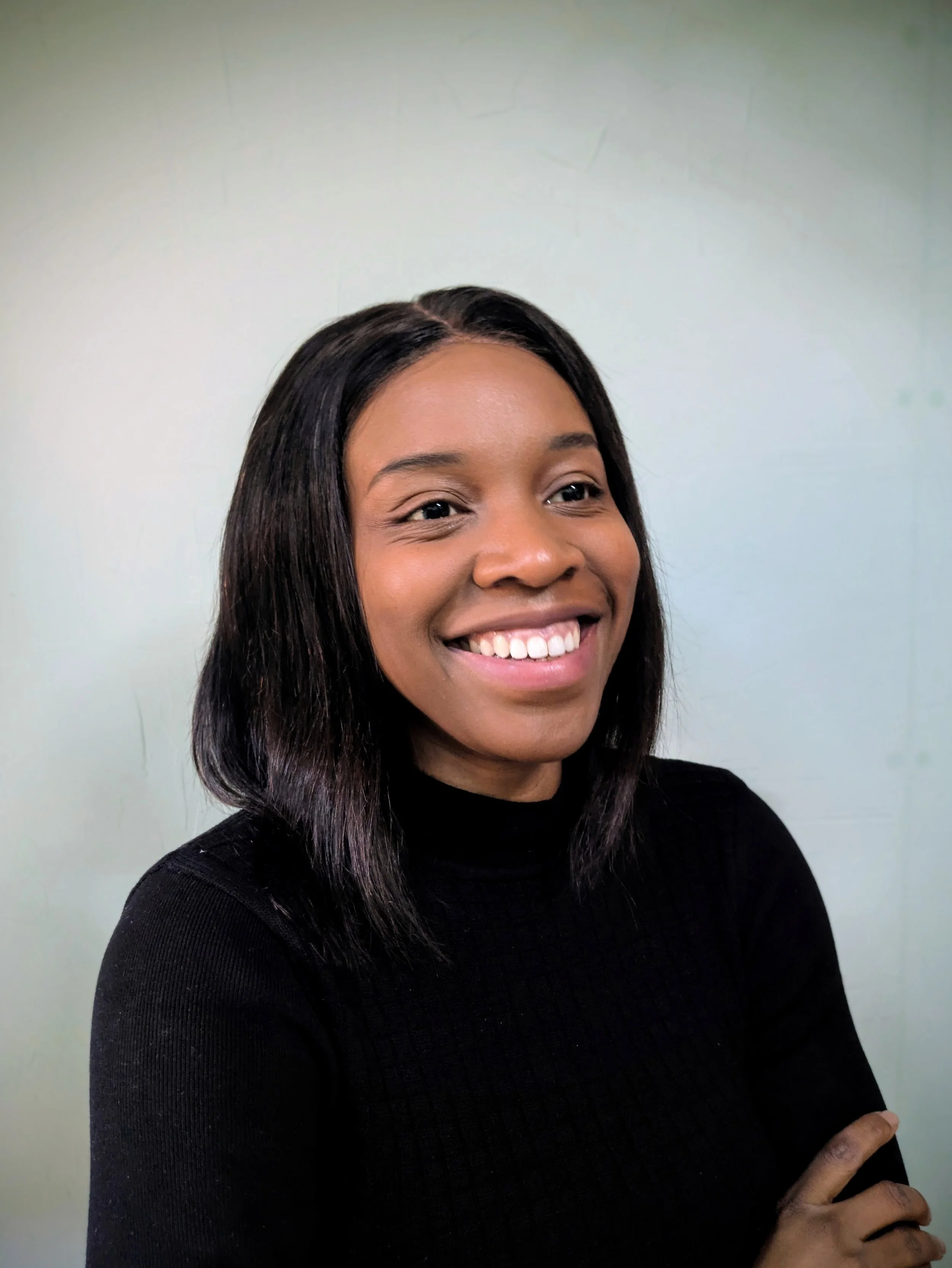 Ope the Tutor with shoulder-length black hair wearing a black turtleneck, smiling during an online chemistry lesson with an  A-Level student