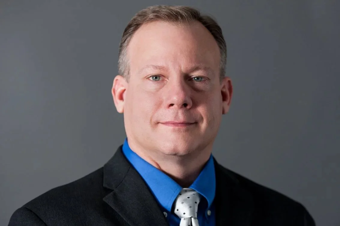 Professional man in a suit and tie against a gray background.