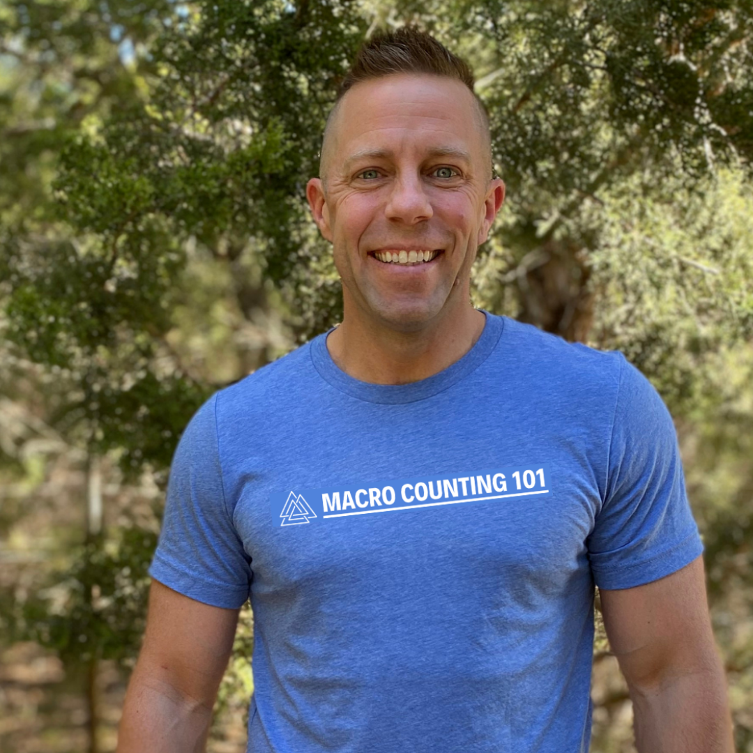 A smiling man outdoors wearing a blue T-shirt with 'MACRO COUNTING 101' printed on it, standing in front of a background of green trees.