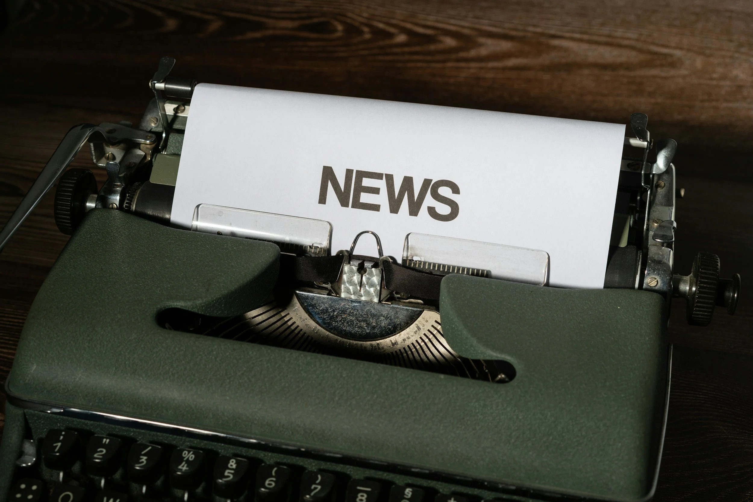 A vintage typewriter with a piece of paper that has the word 'NEWS' typed on it, placed on a wooden surface.