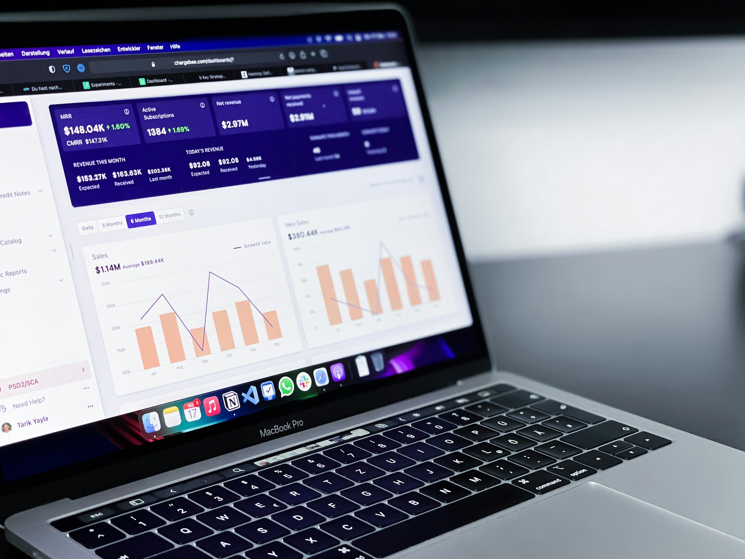 A MacBook Pro laptop displaying a data analytics dashboard with graphs, charts, and statistics, on a desk with a white wall in the background.