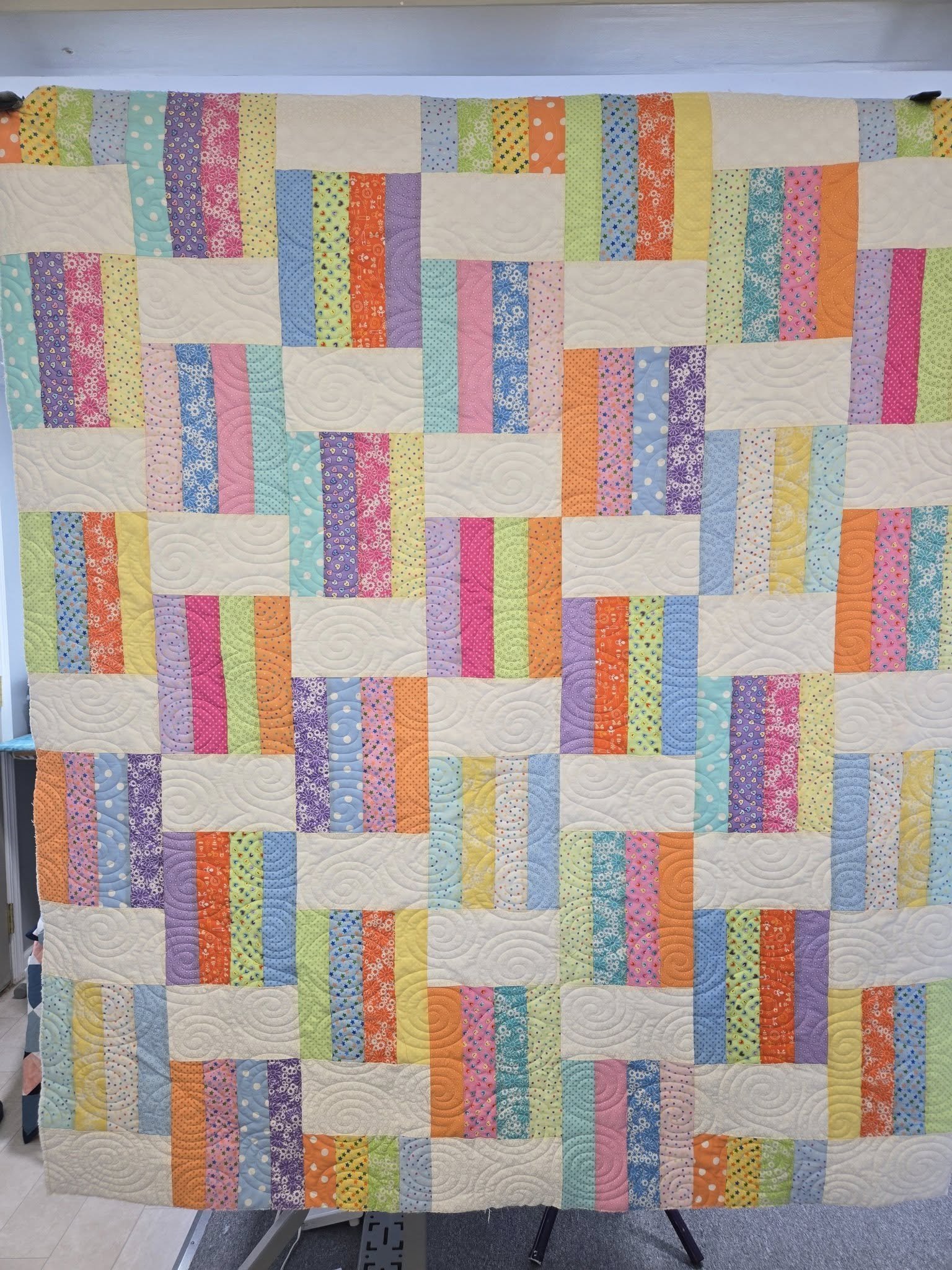 Colorful patchwork quilt with various patterned fabric strips in pastel and bright colors, arranged in a grid pattern.
