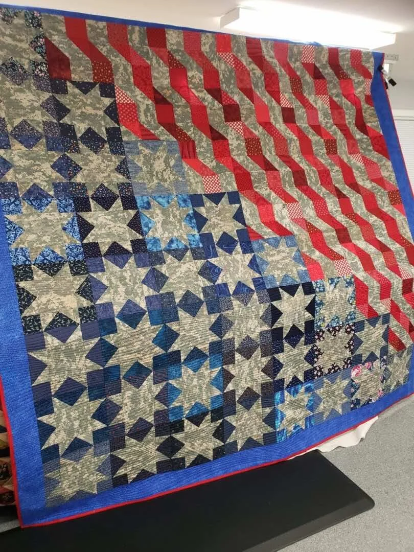 A quilt with an American flag design, featuring red and white stripes on the upper right, and blue and white stars on a blue field on the lower left.