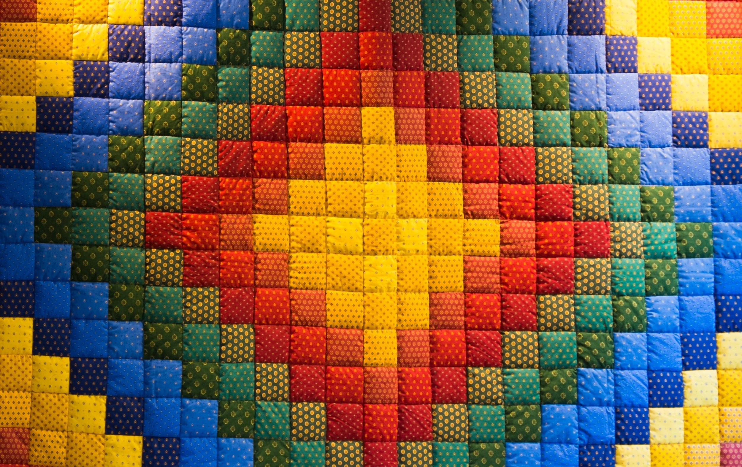 Colorful patchwork quilt with a symmetrical pattern of red, yellow, green, blue, and orange squares with polka dots.