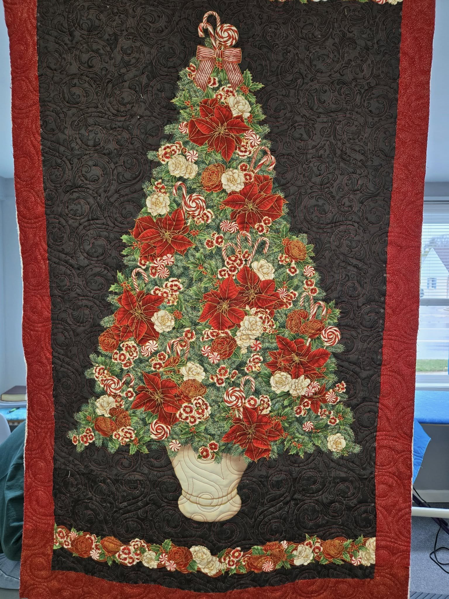 Decorative quilt depicting a Christmas tree made of flowers and candy canes in a vase, with red and green colors, and a floral border.