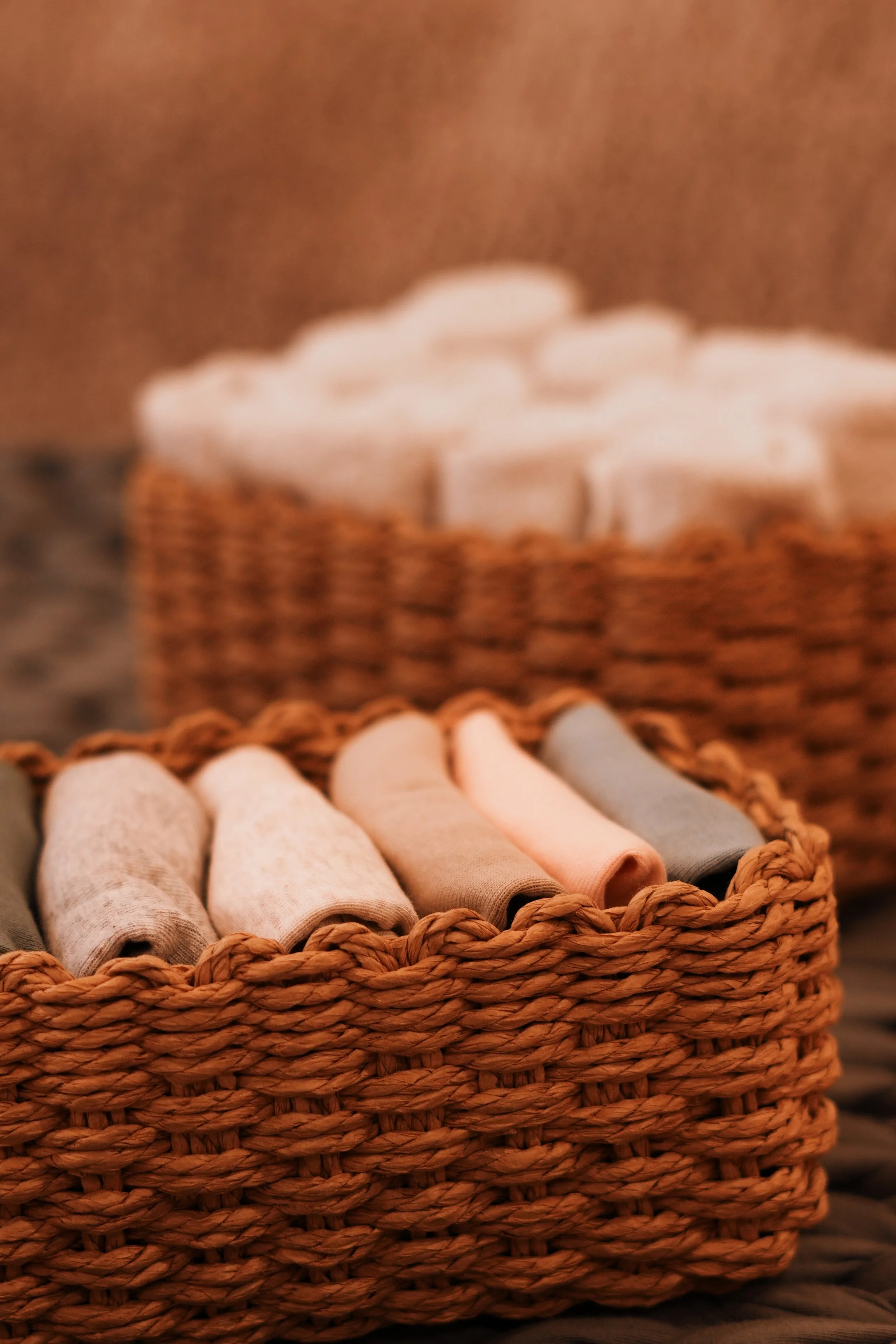 Woven basket with folded multicolored onsies, another basket with white towels in the background.