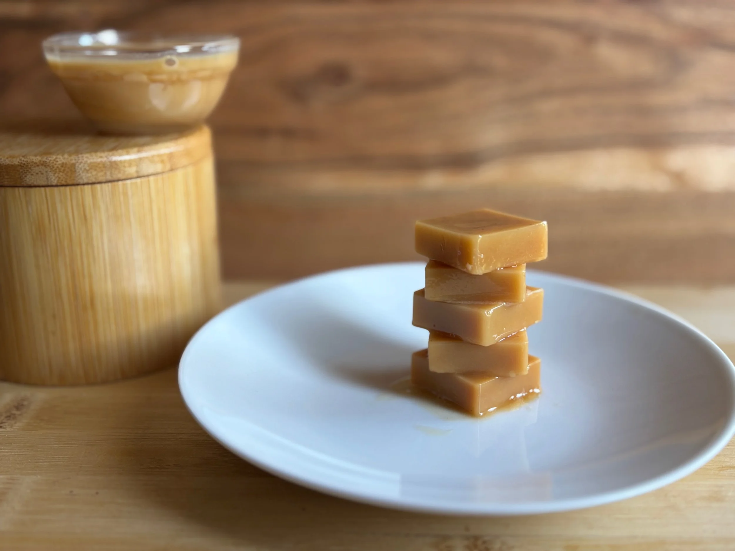 Stack of caramel-colored fudge squares on a white plate with a wooden surface in the background.