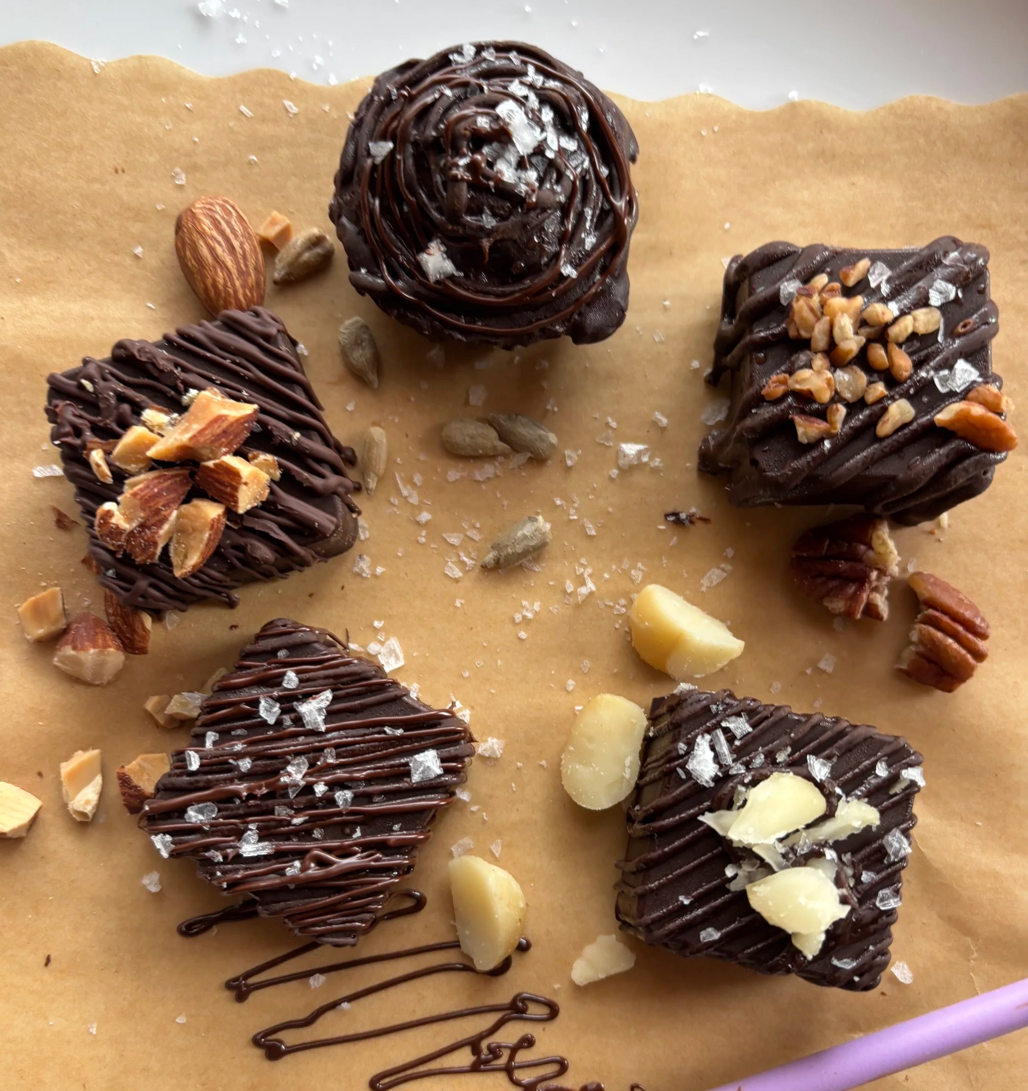 Group of assorted chocolates topped with nuts and sea salt on a sheet of parchment paper.