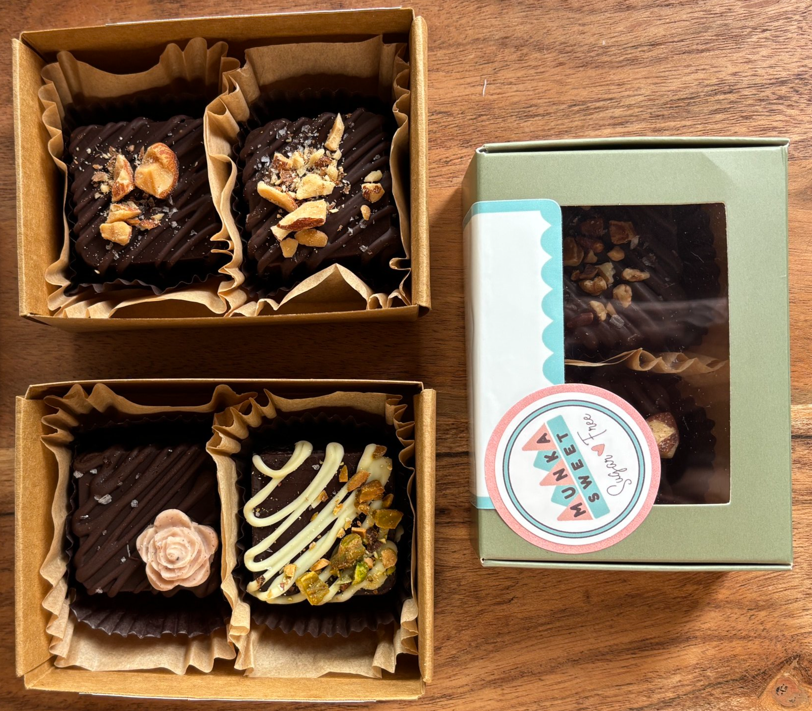 Three boxes of assorted chocolates with toppings such as nuts, flower-shaped, white drizzle, and sprinkled salt, on a wooden surface.