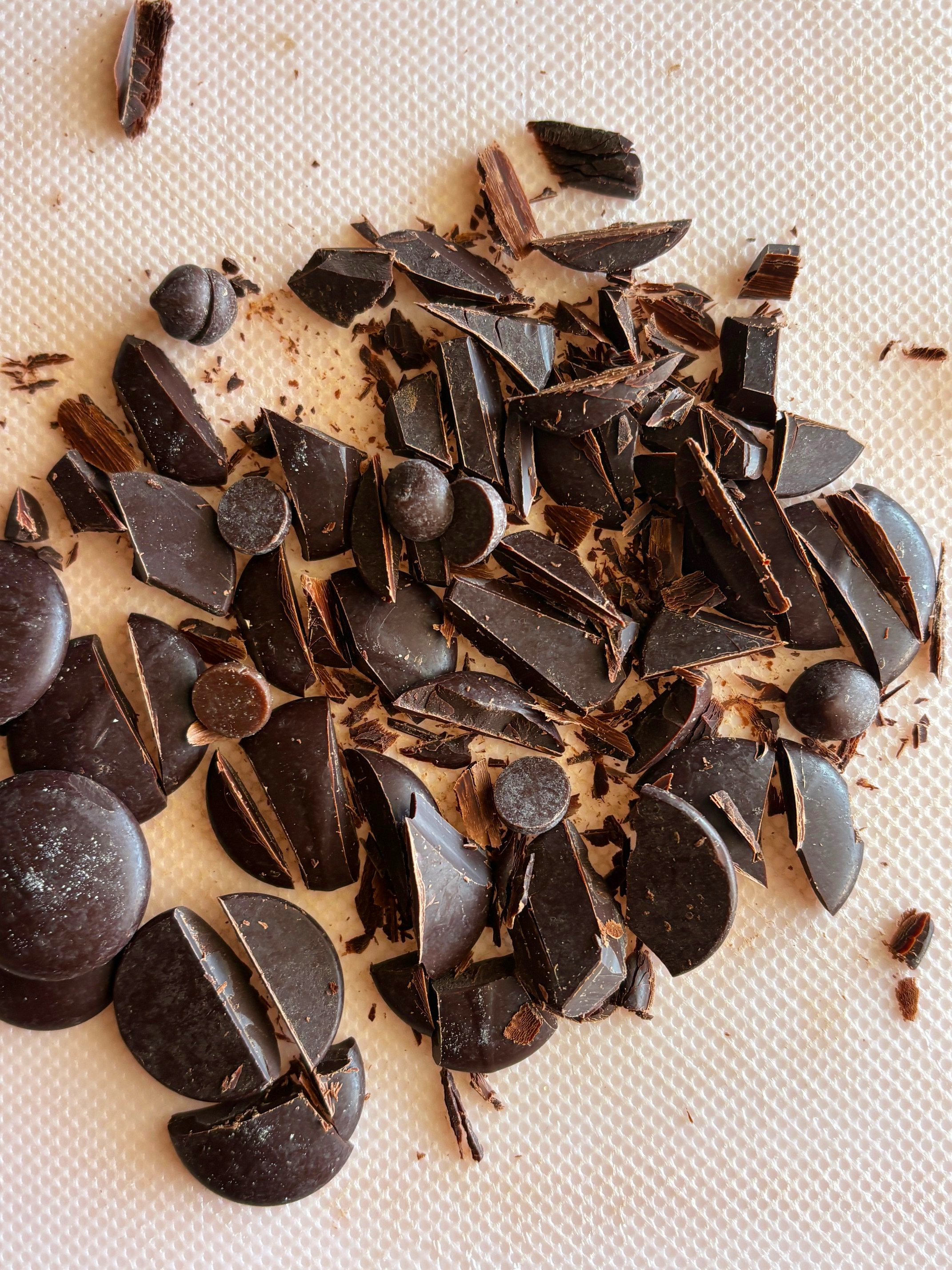Broken dark chocolate pieces and chocolate chips on a white textured surface.