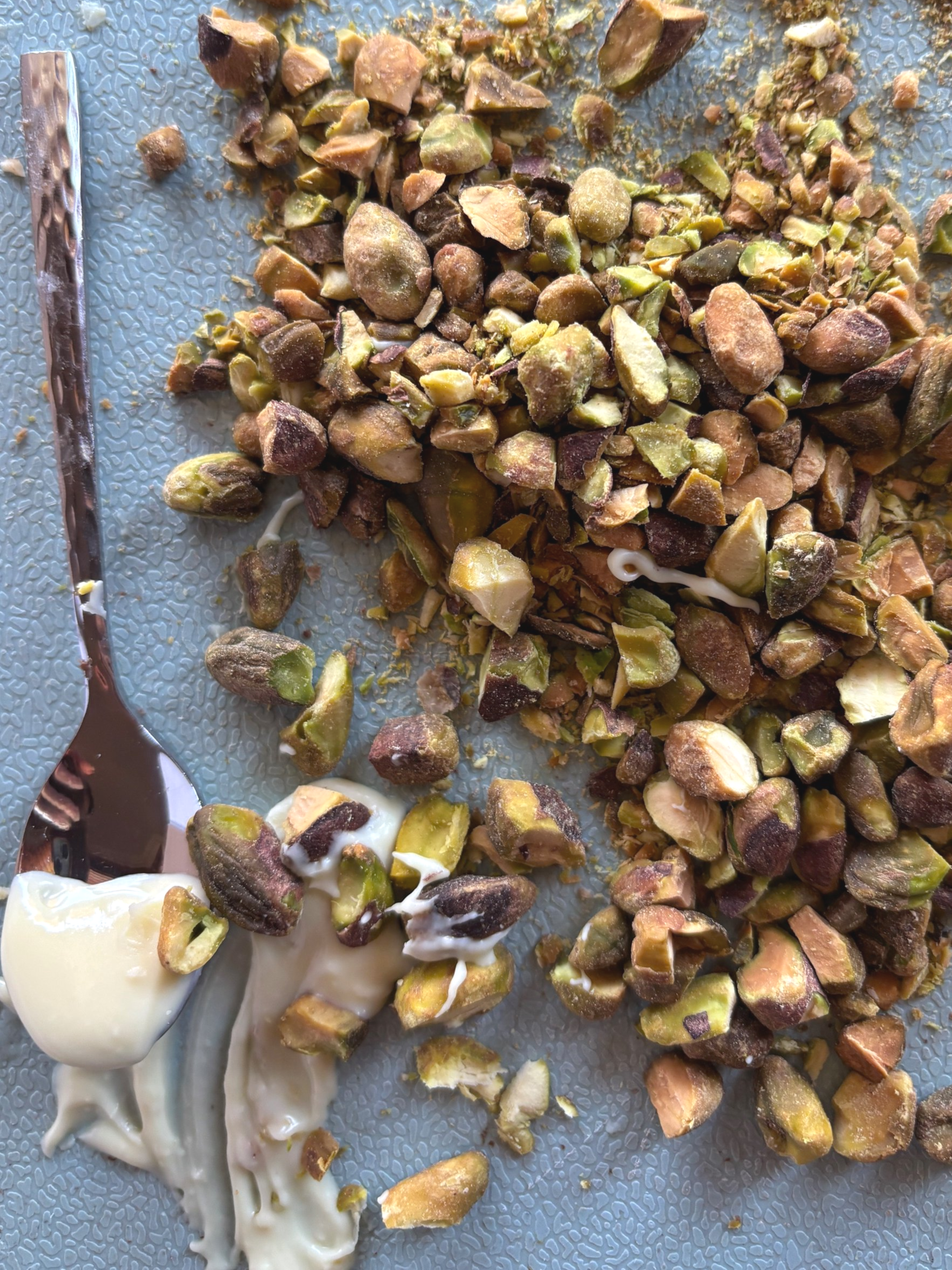 Chopped pistachio nuts on a light blue textured surface with a dollop of white creamy yogurt or sauce.