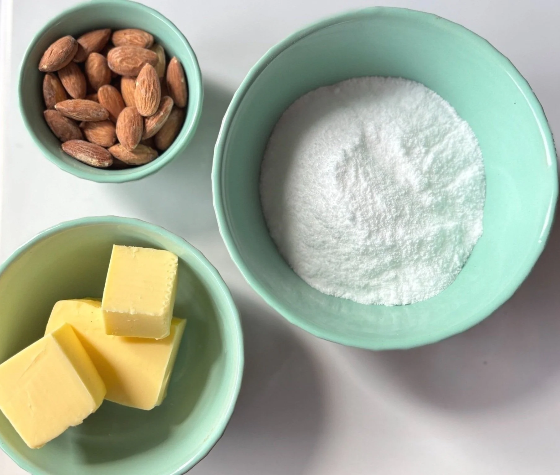 Three green bowls containing almonds, sugar, and butter cubes.