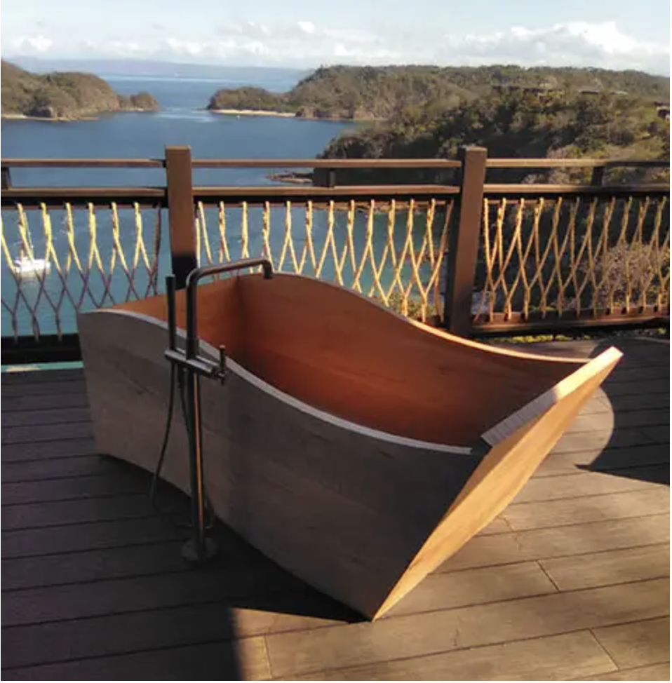 Wooden bathtub on a deck overlooking a body of water and islands in a scenic landscape.