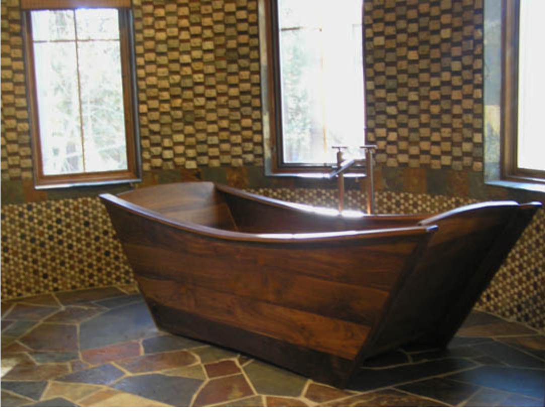 Wooden bathtub inside a room with patterned walls and stone tile floor, illuminated by natural light from three windows.