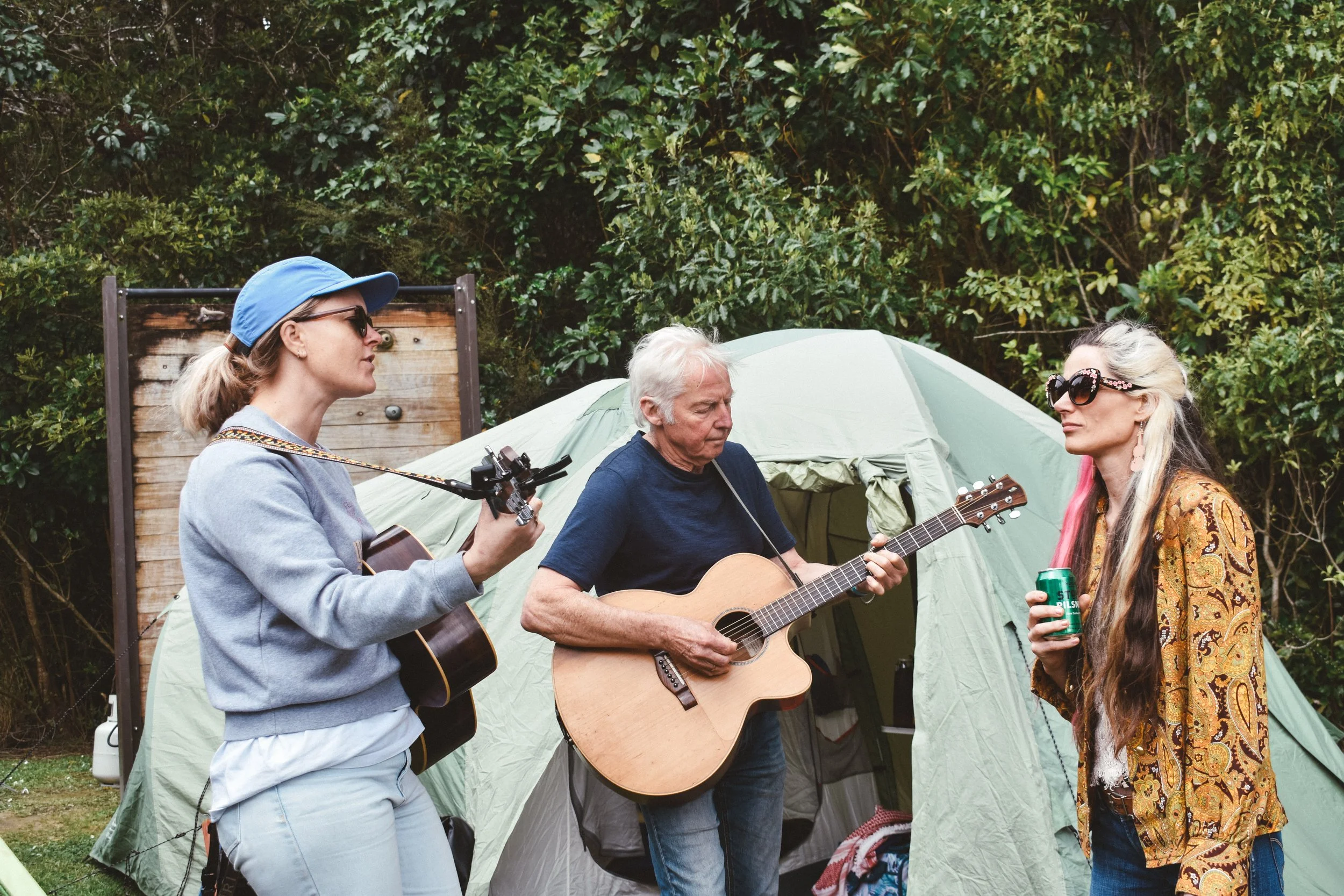 Three people playing and enjoying music near a camping tent outdoors.