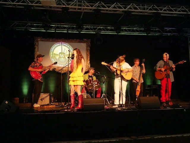 Six young musicians playing instruments on stage, including guitars, drums, and a keyboard, during a live performance.