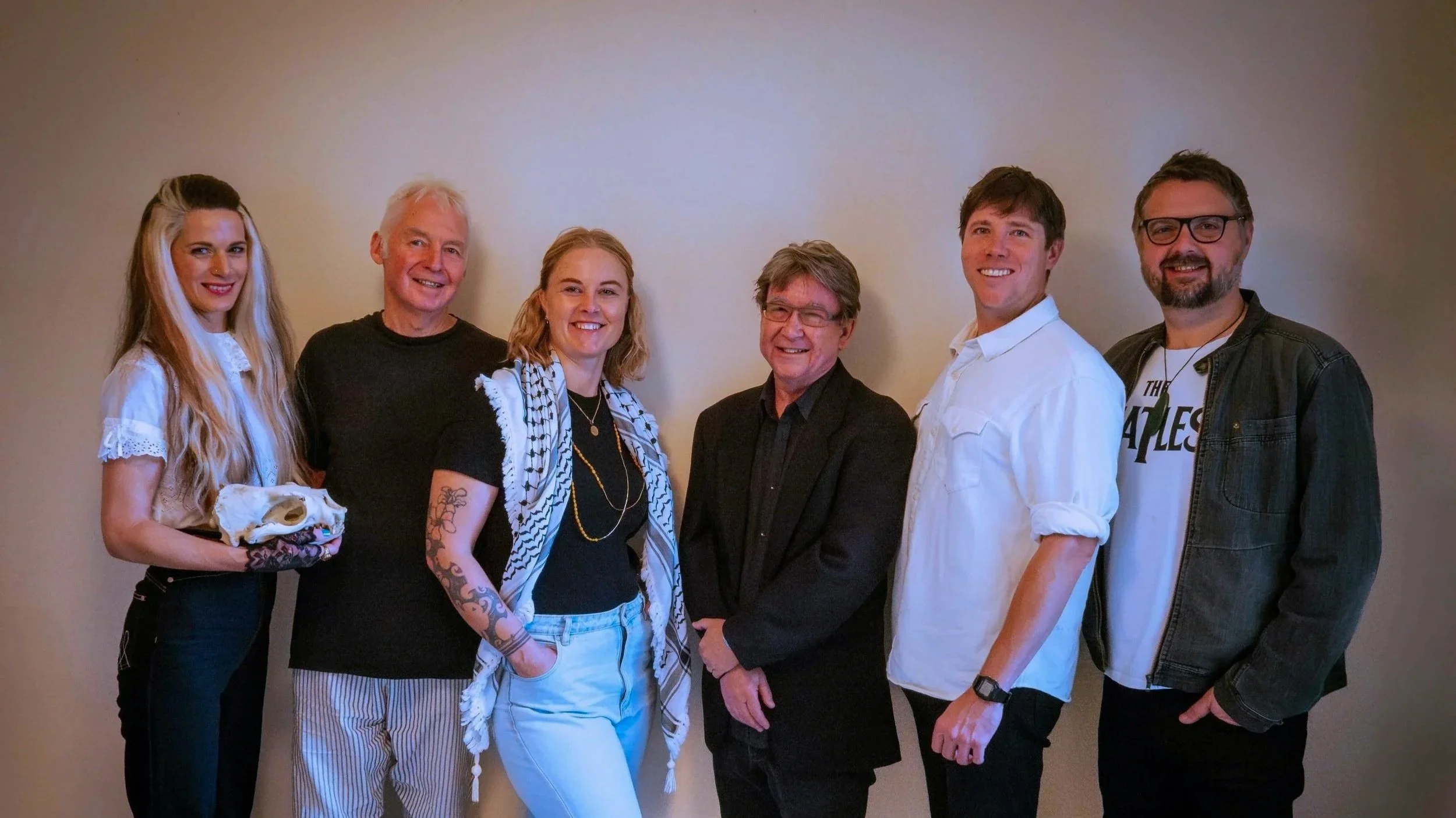 Group of six people standing in a line against a plain background, smiling and posing for the photo.