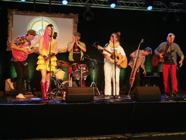 Band performing on stage with seven members, including guitarists, a drummer, and a vocalist, at a music event.