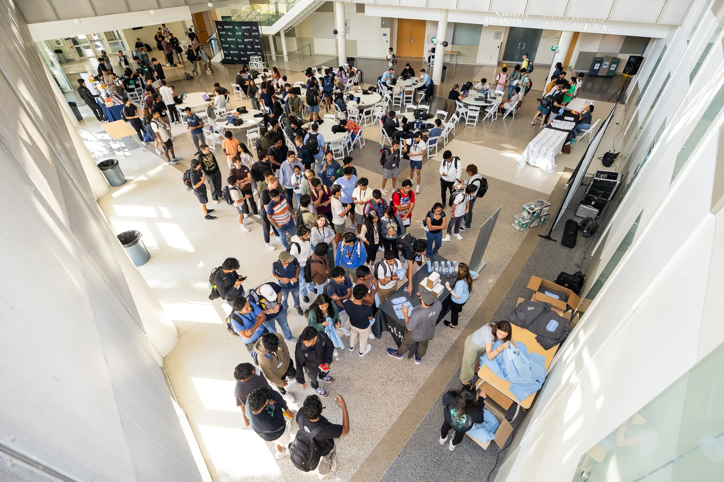 Crowd of students lining up at registration table in a large, modern university lobby with tables, chairs, and informational booths.