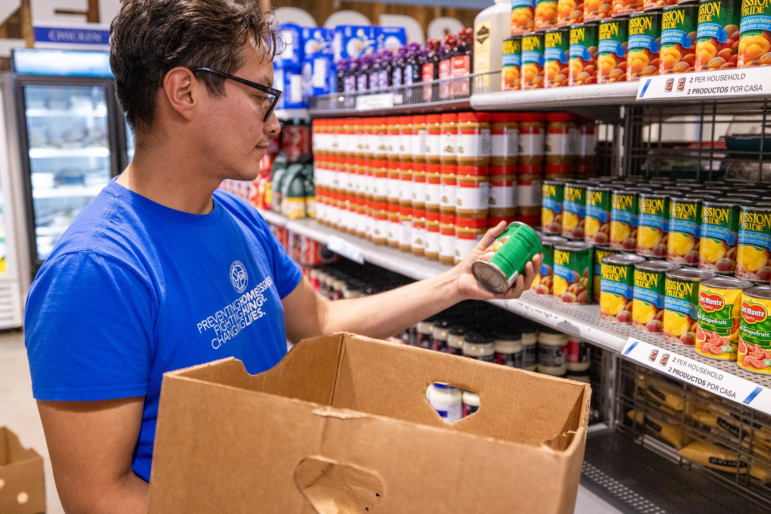 A person shopping at a grocery store, holding a canned food item in front of shelves stocked with canned fruits.