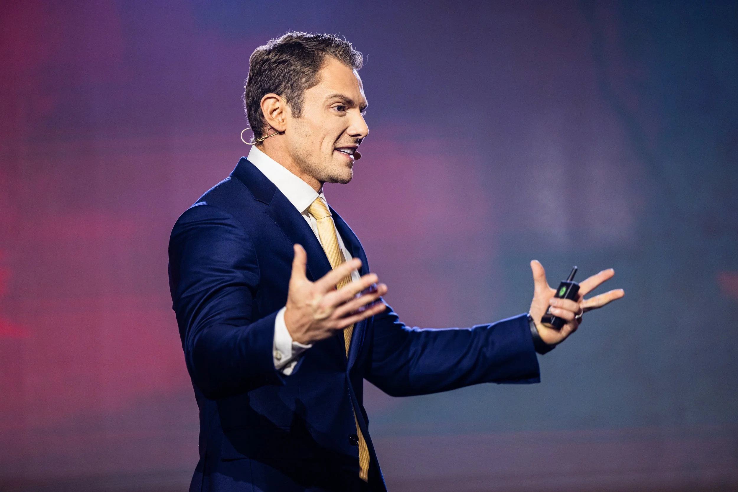 Man in navy suit giving a presentation with a microphone headset.