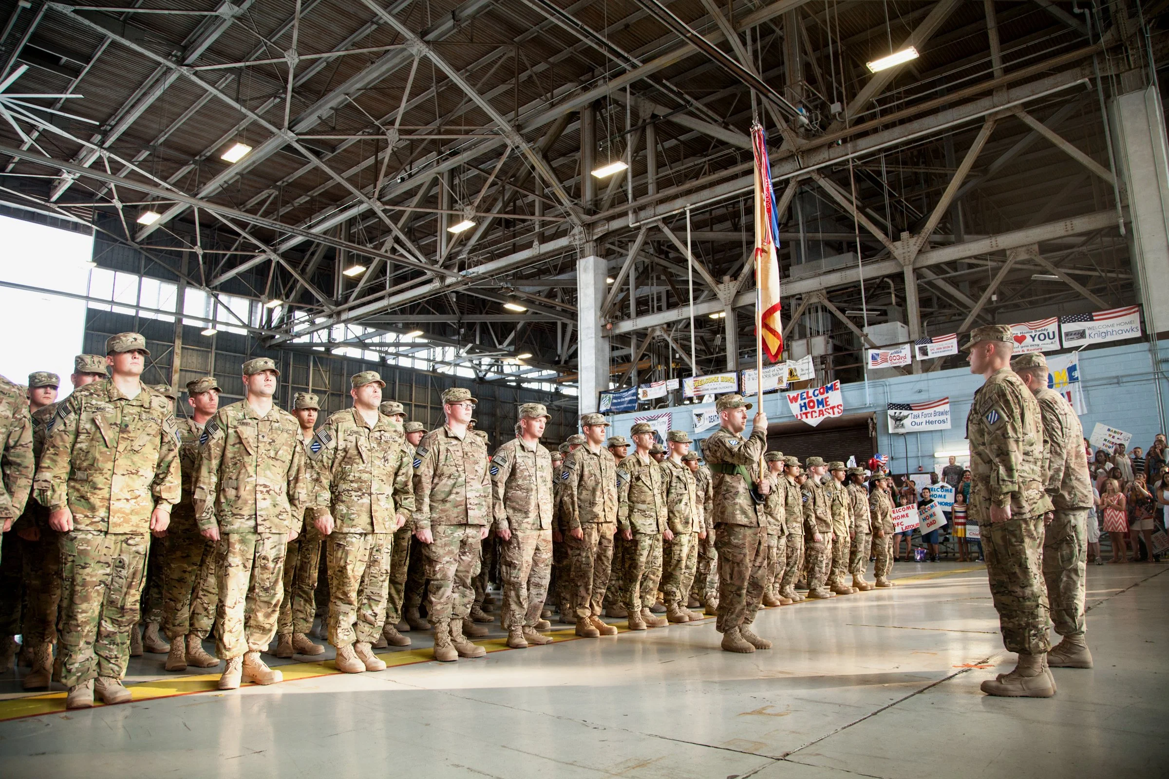Silhouetted US Army troops standing in formation inside a hangar at Hunter Army Airfield in Savannah during a military homecoming ceremony, captured in a documentary photography style by jm photographics.