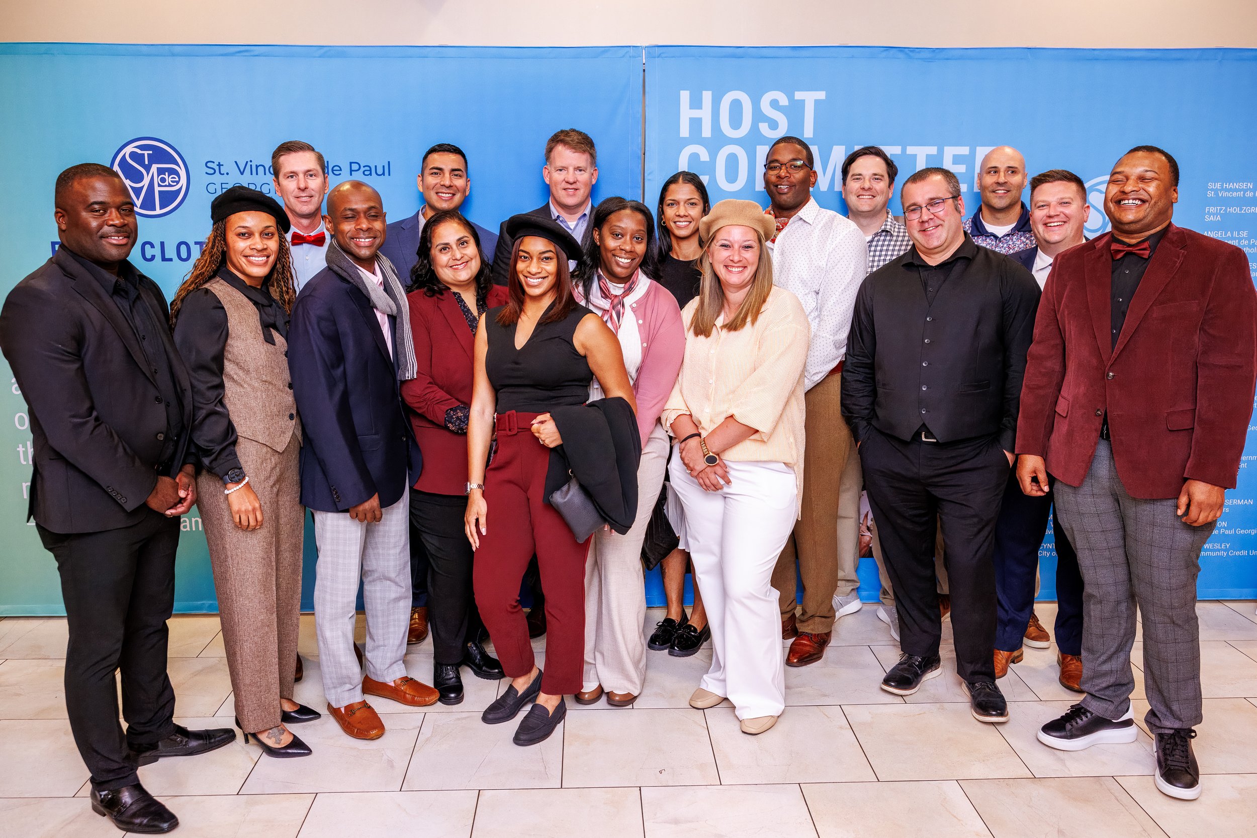 Group of diverse professionals smiling at an indoor event, standing in front of a blue backdrop with text and logos.