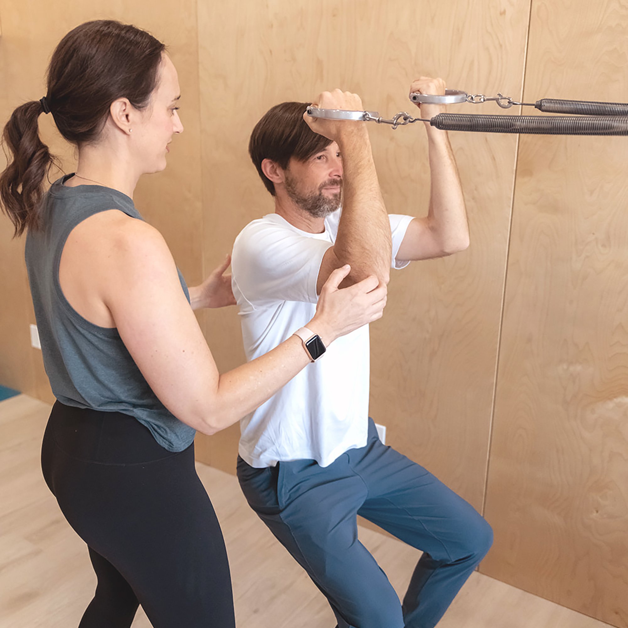 A man using a suspension trainer with assistance from a Jenny.