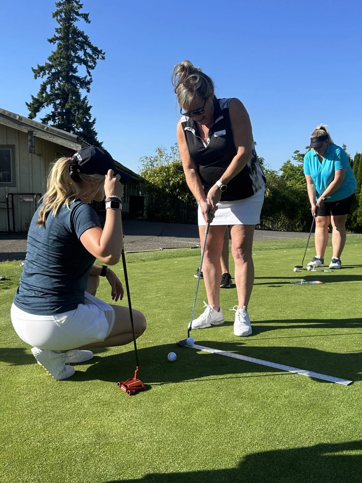 Women and girl practicing putting on a golf course, with tools and golf balls.