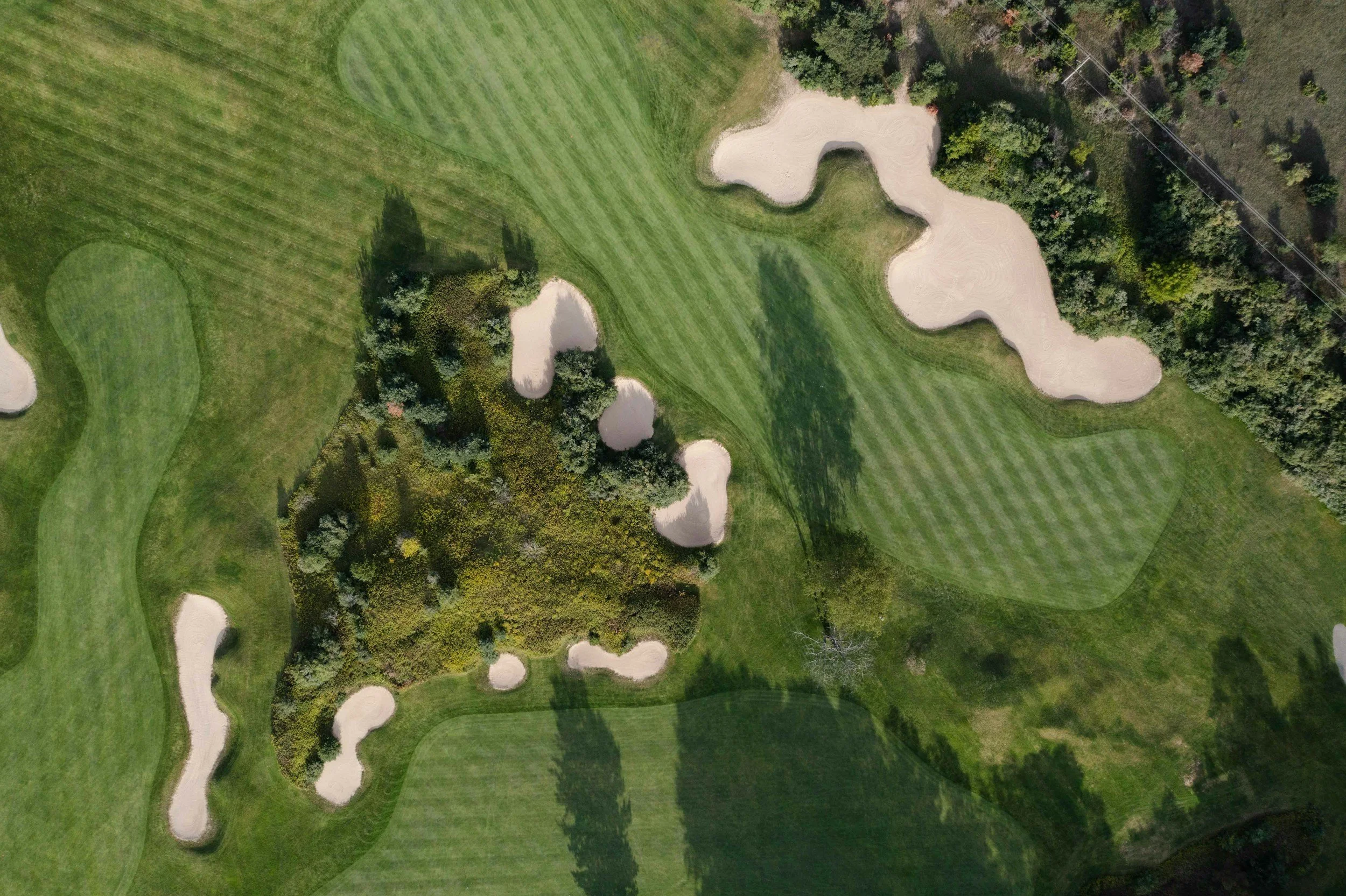 Aerial view of a golf course with multiple sand traps and green fairways, surrounded by trees and shrubbery.