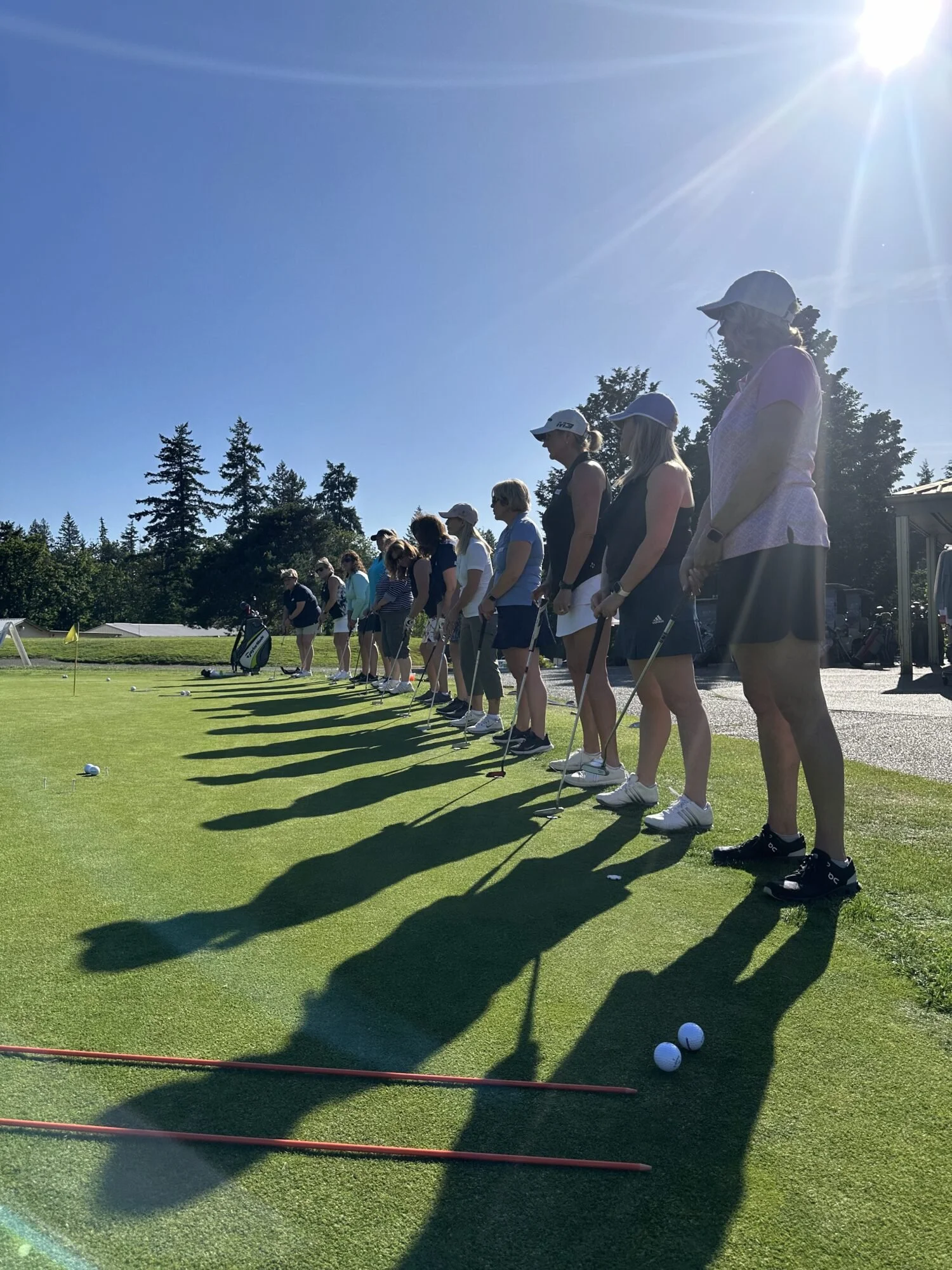 A group of women standing in a row on a golf course preparing to tee off on sunny day.