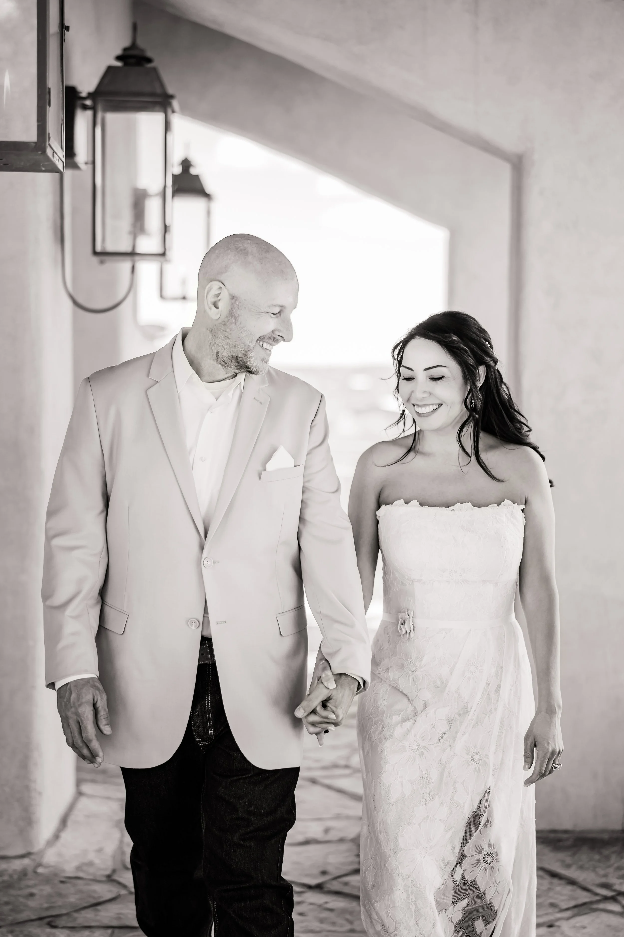 A man and woman walking hand in hand, smiling at each other, in a stylish outdoor setting.