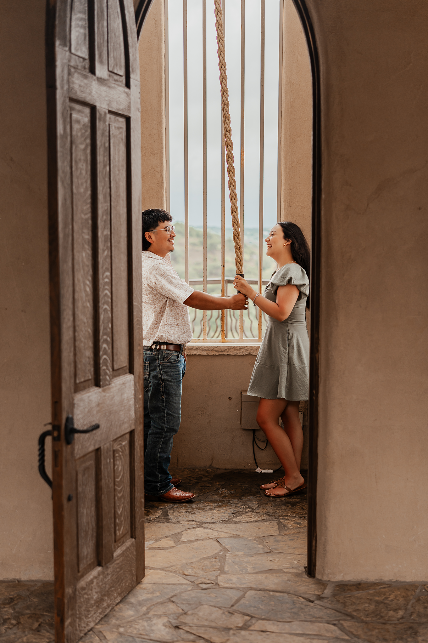 A man and woman sharing a joyful moment on a swing, seen through an open wooden door.