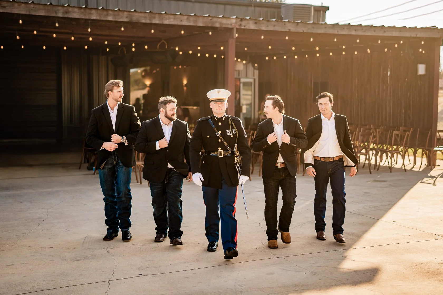 A group of five men walking together outdoors, with one dressed in a military uniform and the others in suits, during sunset.