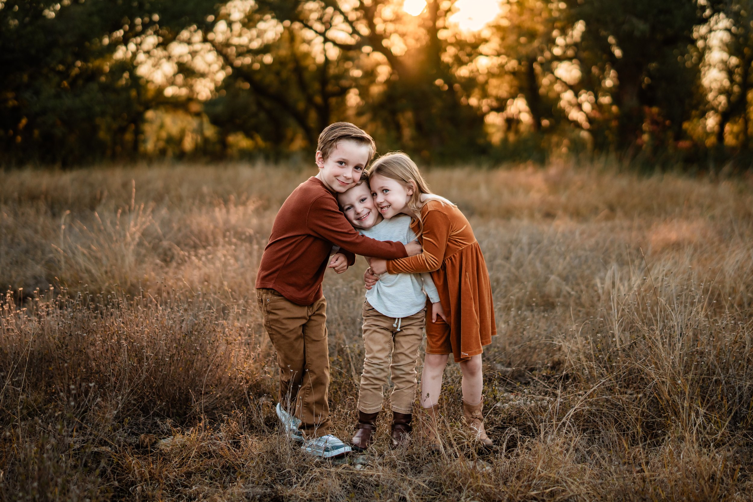 Four children hugging and smiling in a field during sunset.